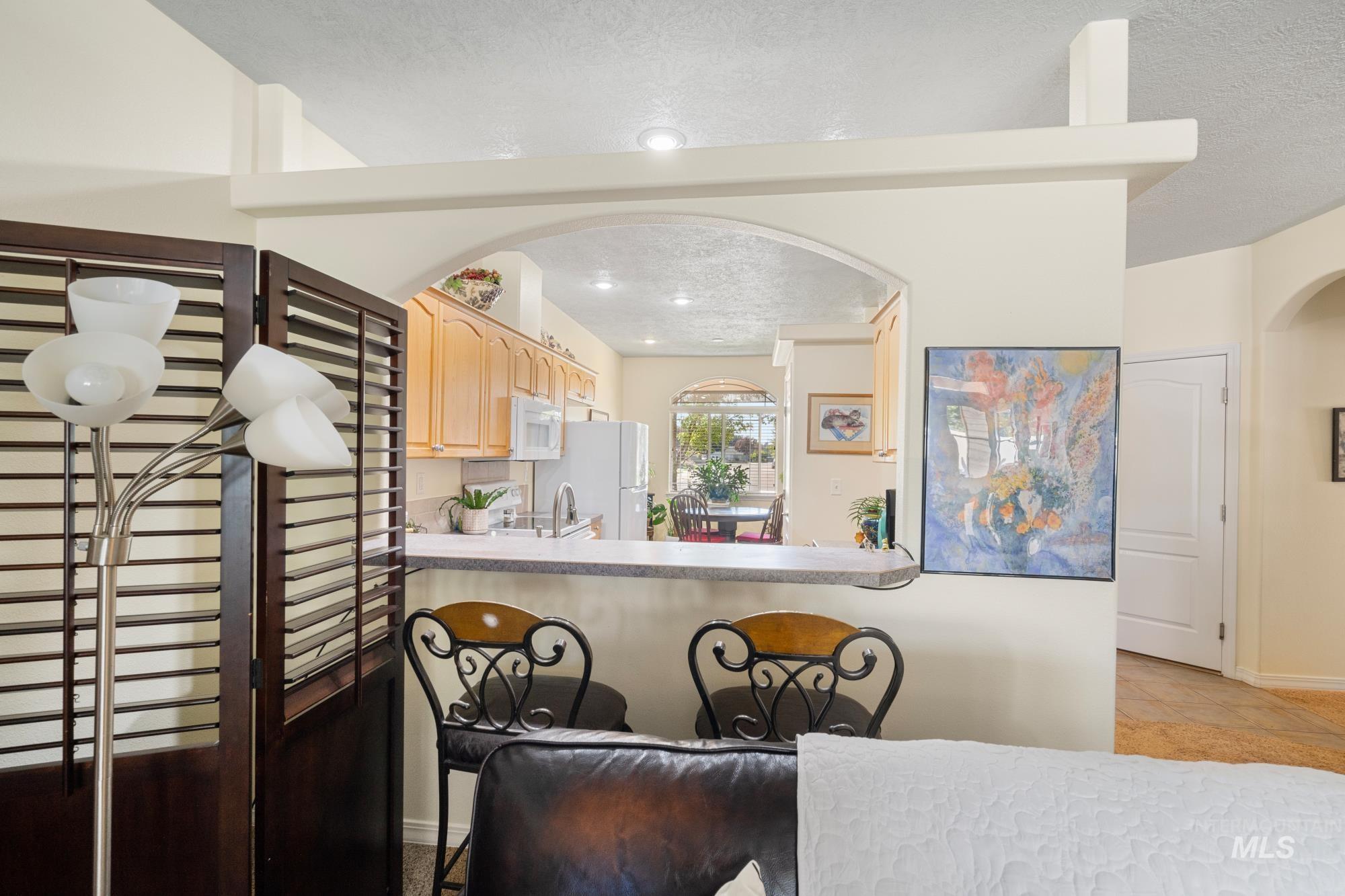 Kitchen featuring a textured ceiling, light brown cabinetry, light countertops, light tile patterned flooring, and arched walkways