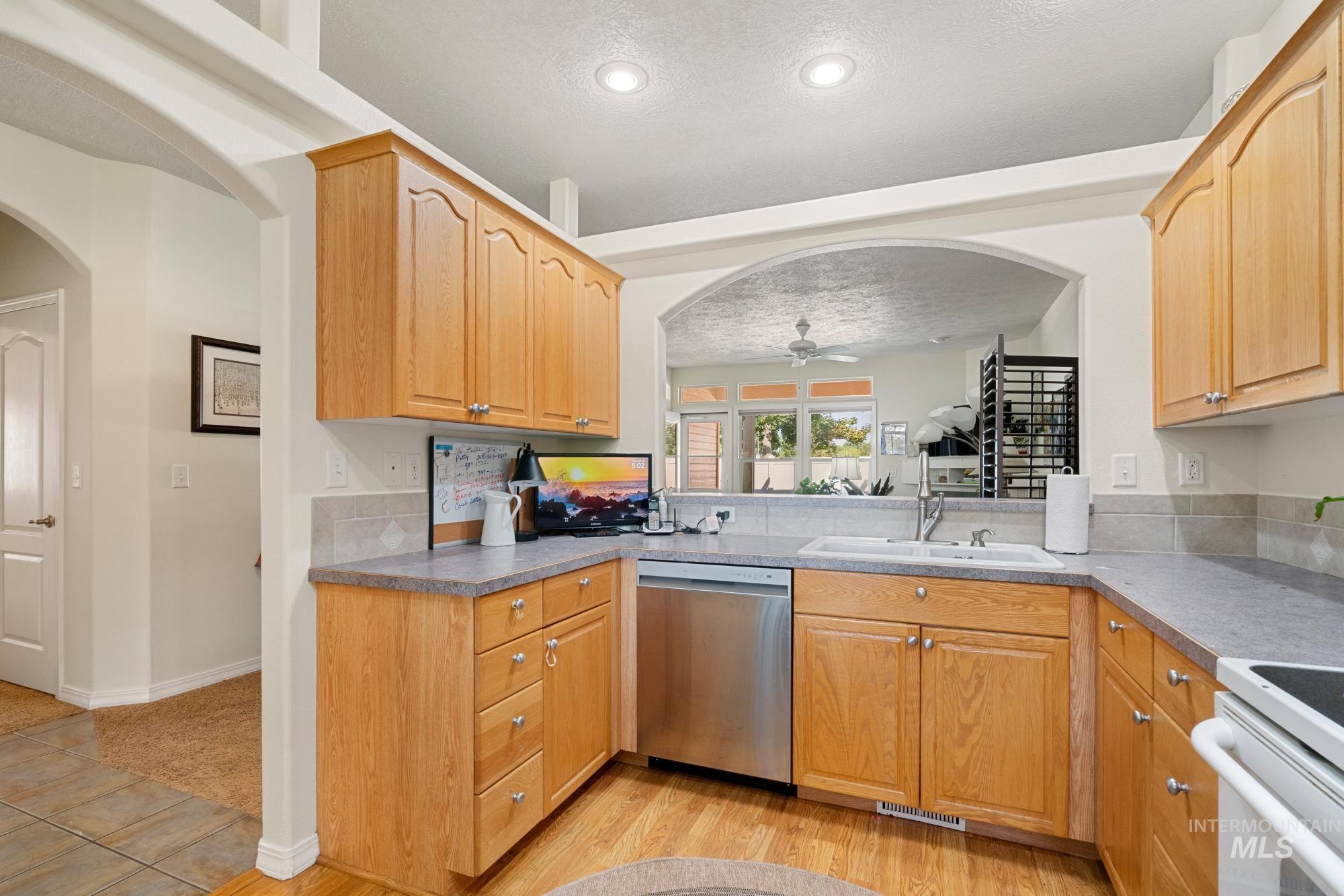 Kitchen featuring arched walkways, stainless steel dishwasher, electric stove, a textured ceiling, and light wood-style floors