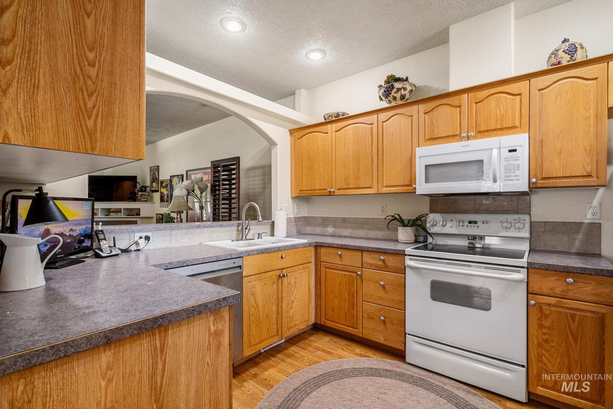 Kitchen featuring white appliances, light wood-style floors, a textured ceiling, dark countertops, and recessed lighting