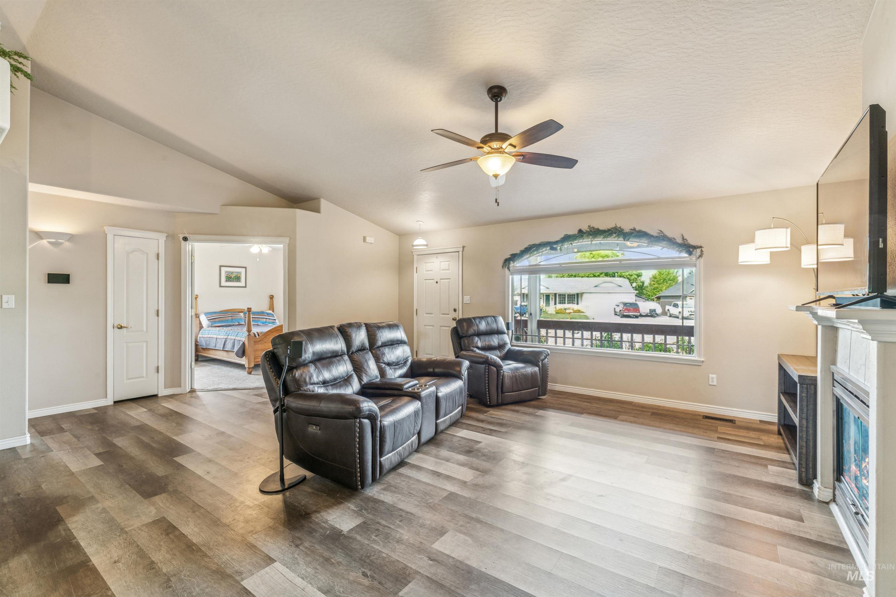 Living room featuring light wood-style floors, vaulted ceiling, a glass covered fireplace, and ceiling fan
