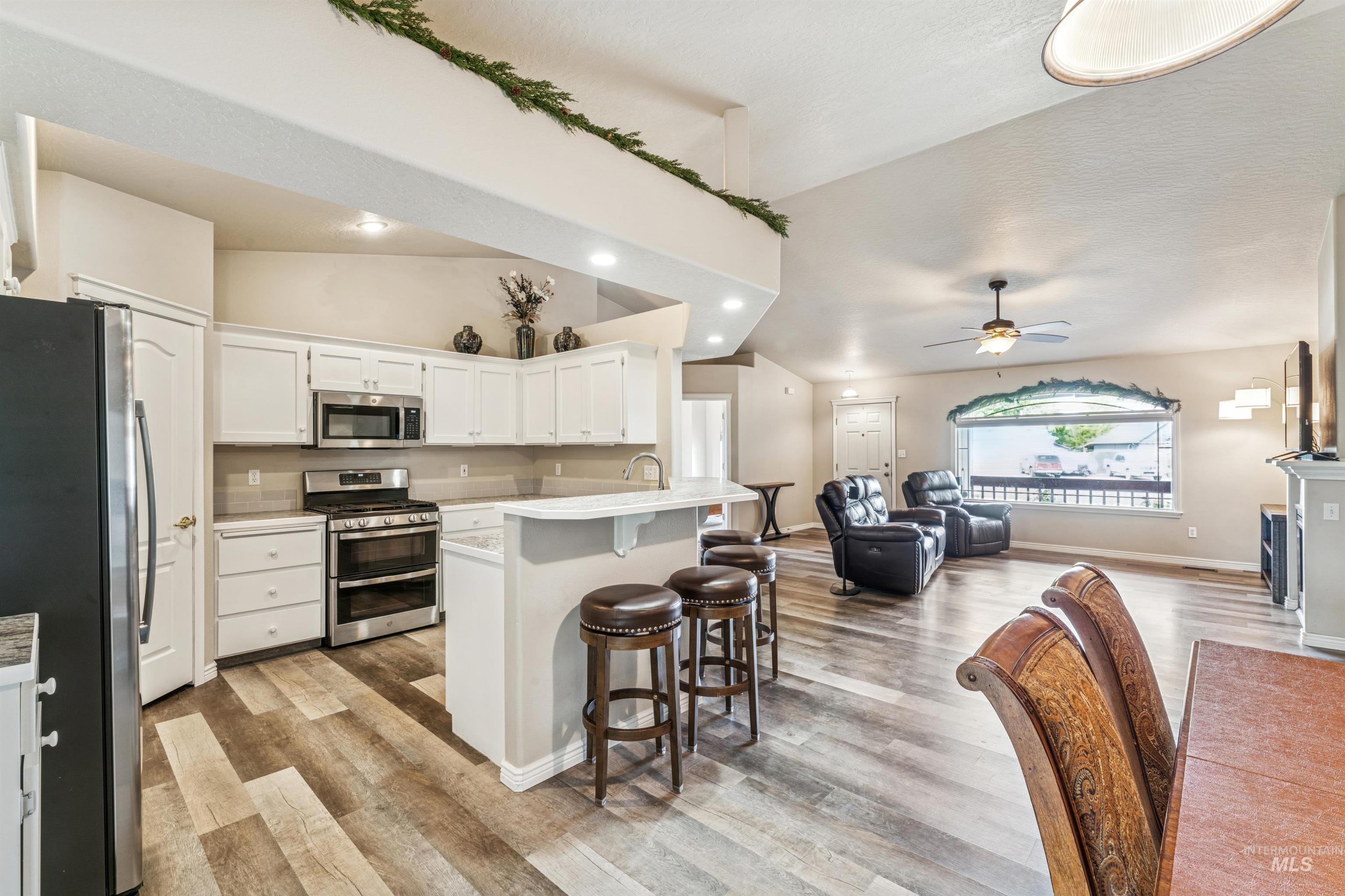Kitchen with white cabinets, stainless steel appliances, open floor plan, light countertops, and a breakfast bar