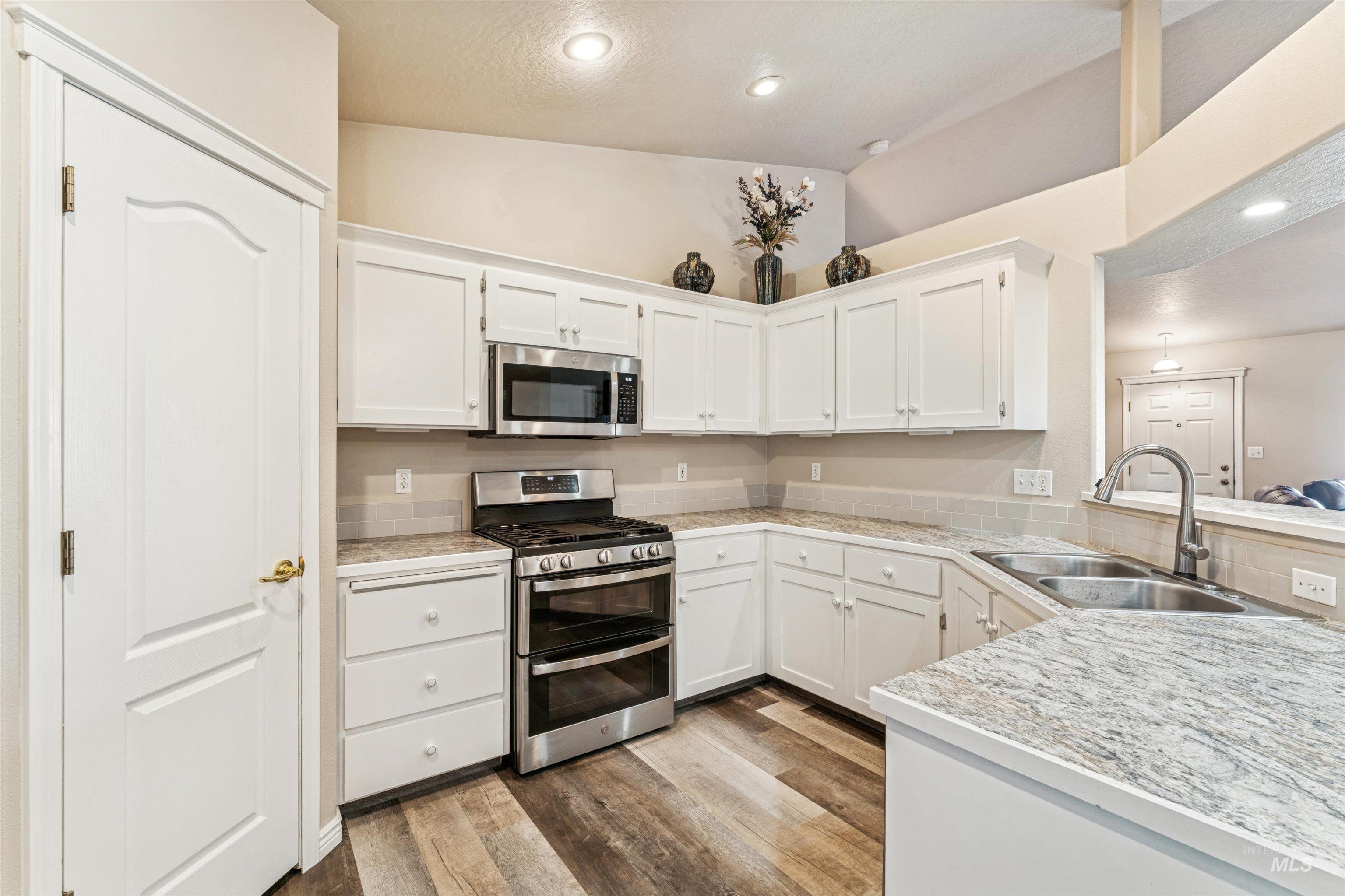 Kitchen featuring appliances with stainless steel finishes, white cabinets, dark wood-style floors, recessed lighting, and lofted ceiling