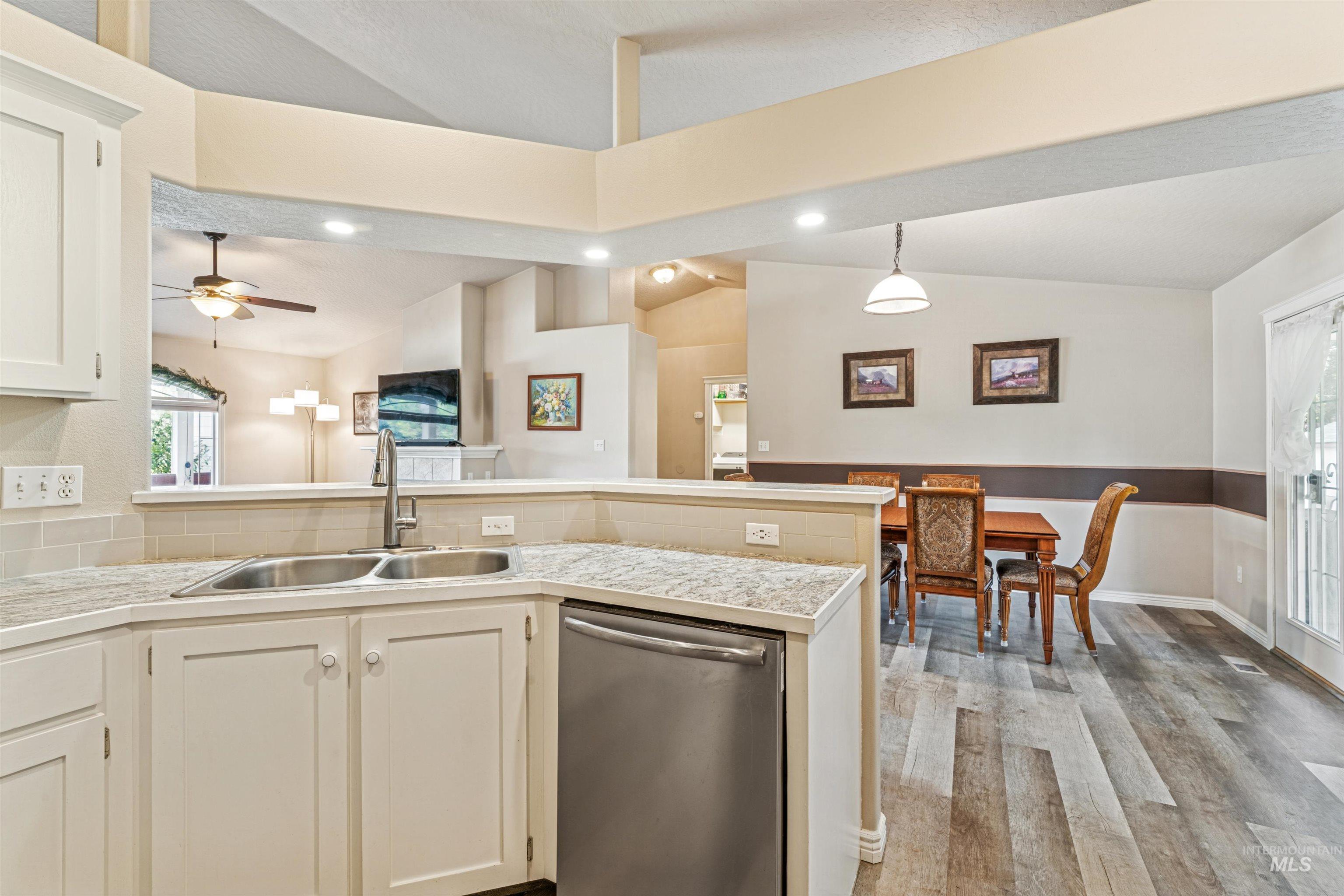 Kitchen featuring stainless steel dishwasher, lofted ceiling, decorative light fixtures, light wood-style flooring, and white cabinets