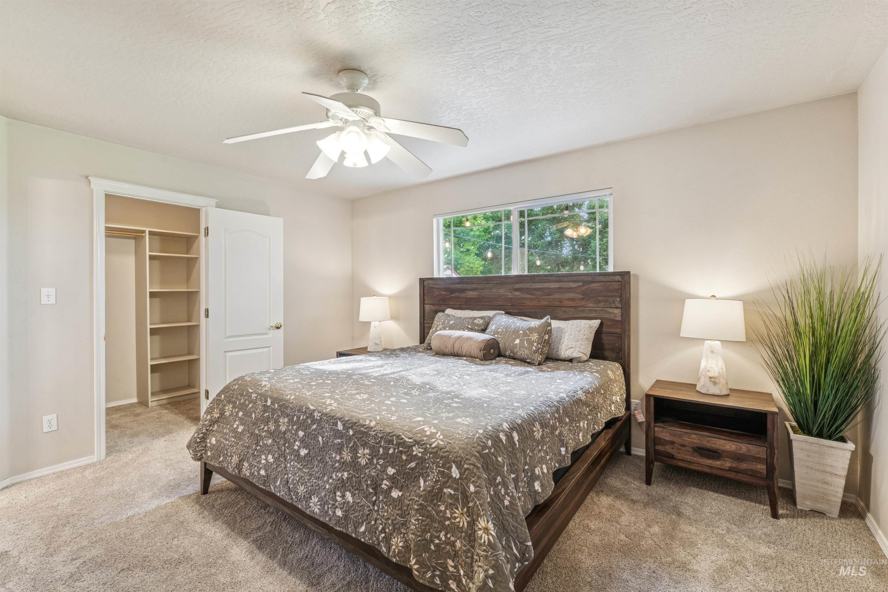 Bedroom featuring light carpet, a textured ceiling, a spacious closet, and a ceiling fan