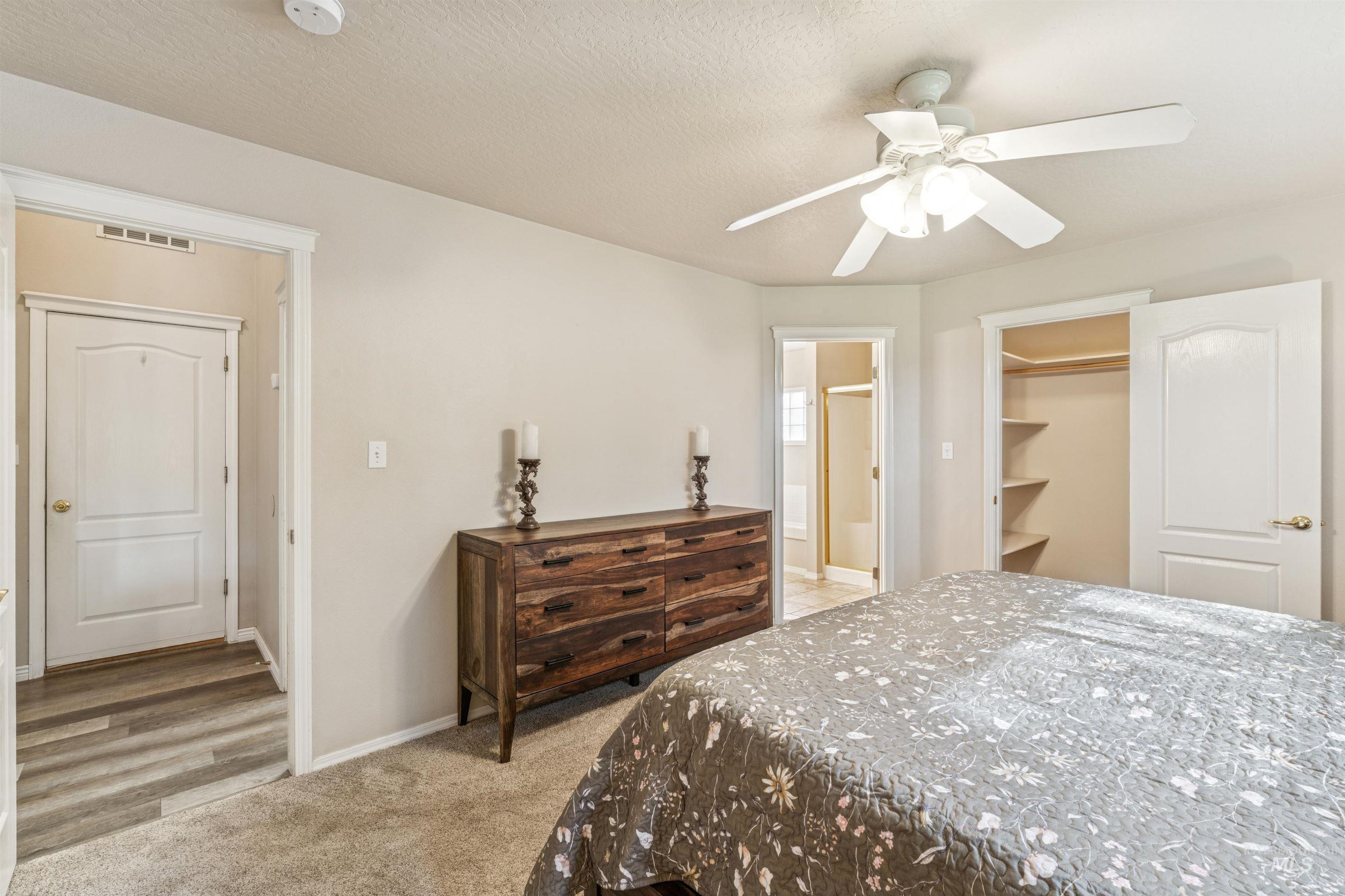 Bedroom with light carpet, a spacious closet, a textured ceiling, ensuite bath, and ceiling fan