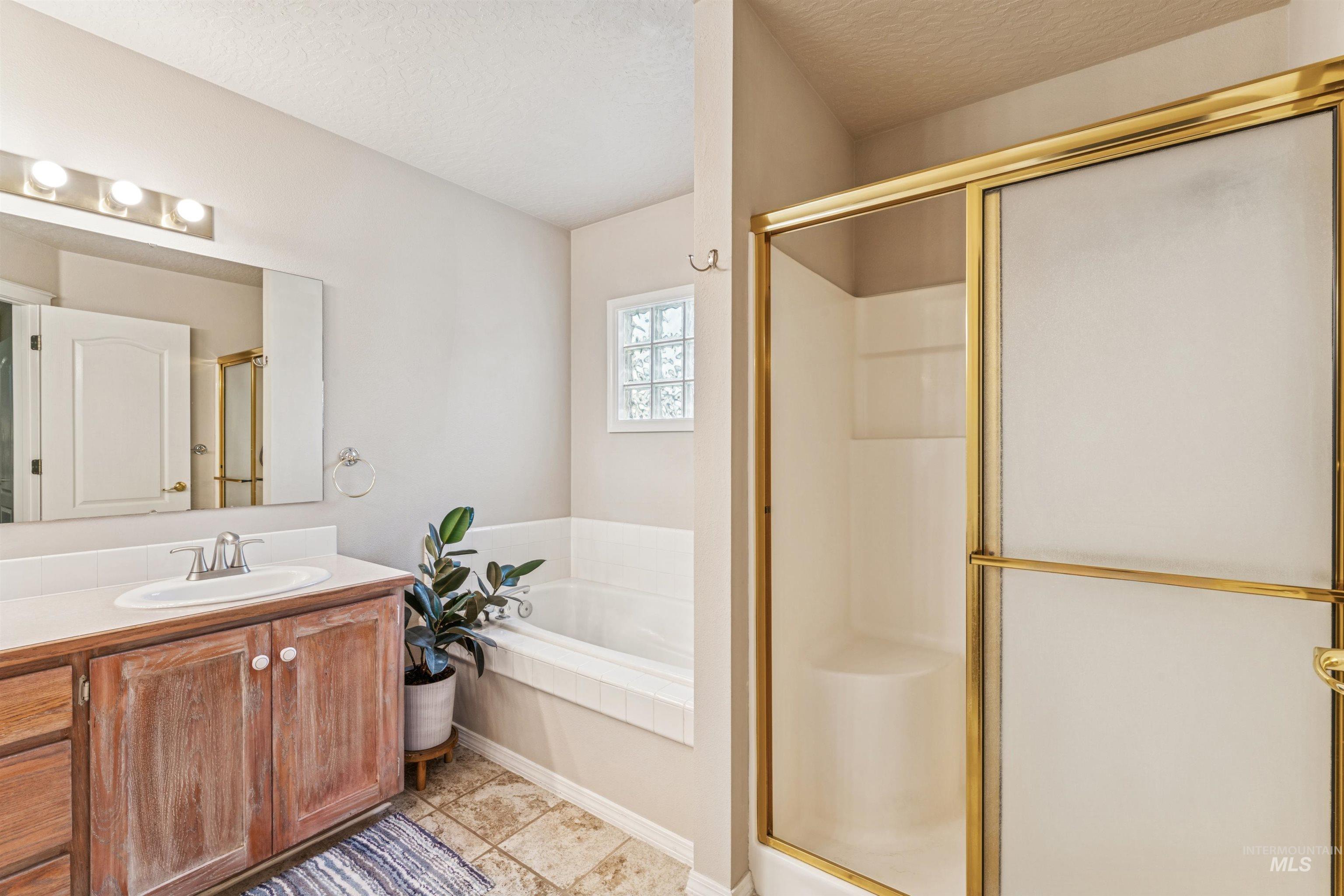 Full bath featuring vanity, a stall shower, a garden tub, a textured ceiling, and light tile patterned flooring