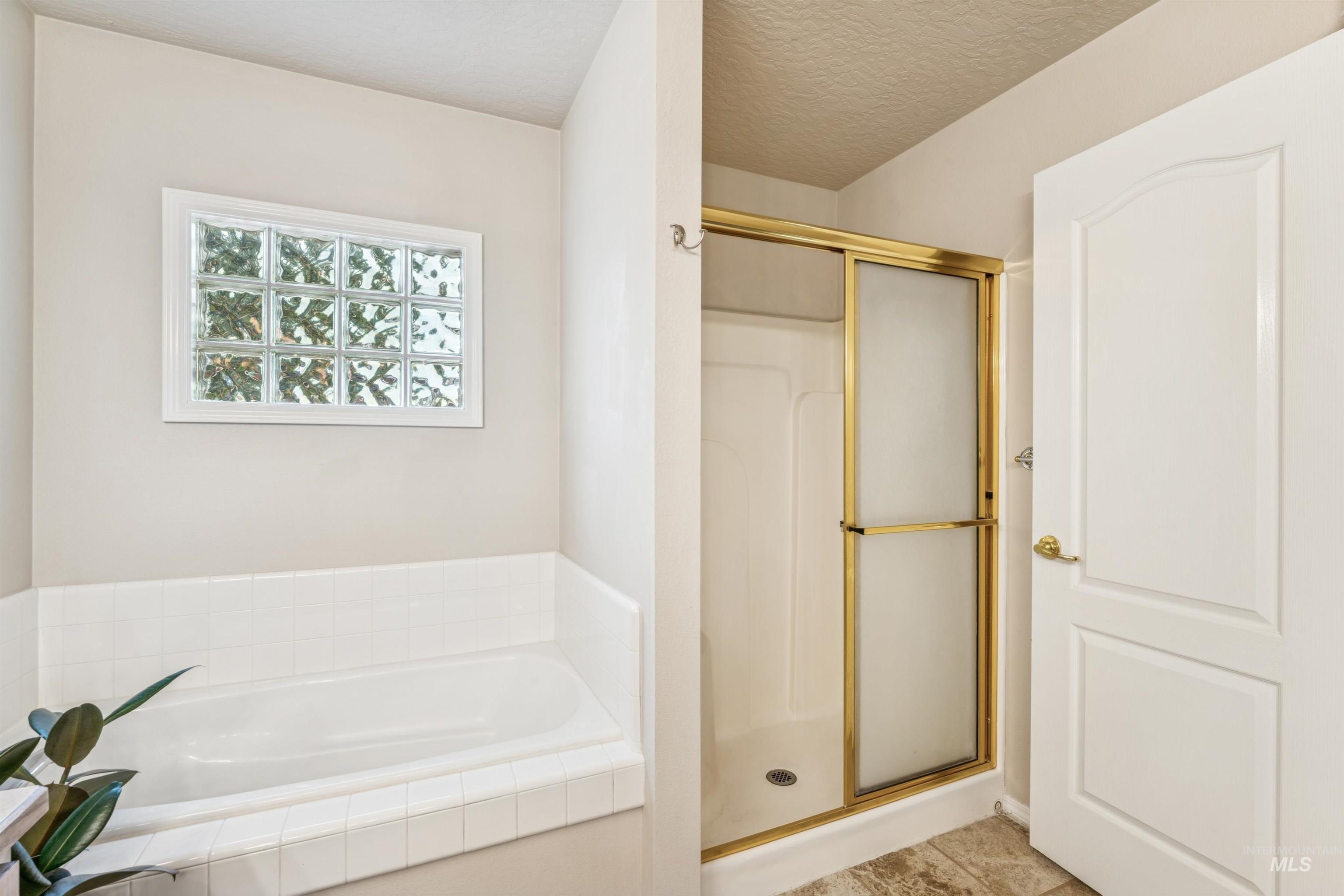 Bathroom featuring a stall shower, a garden tub, a textured ceiling, and light tile patterned flooring