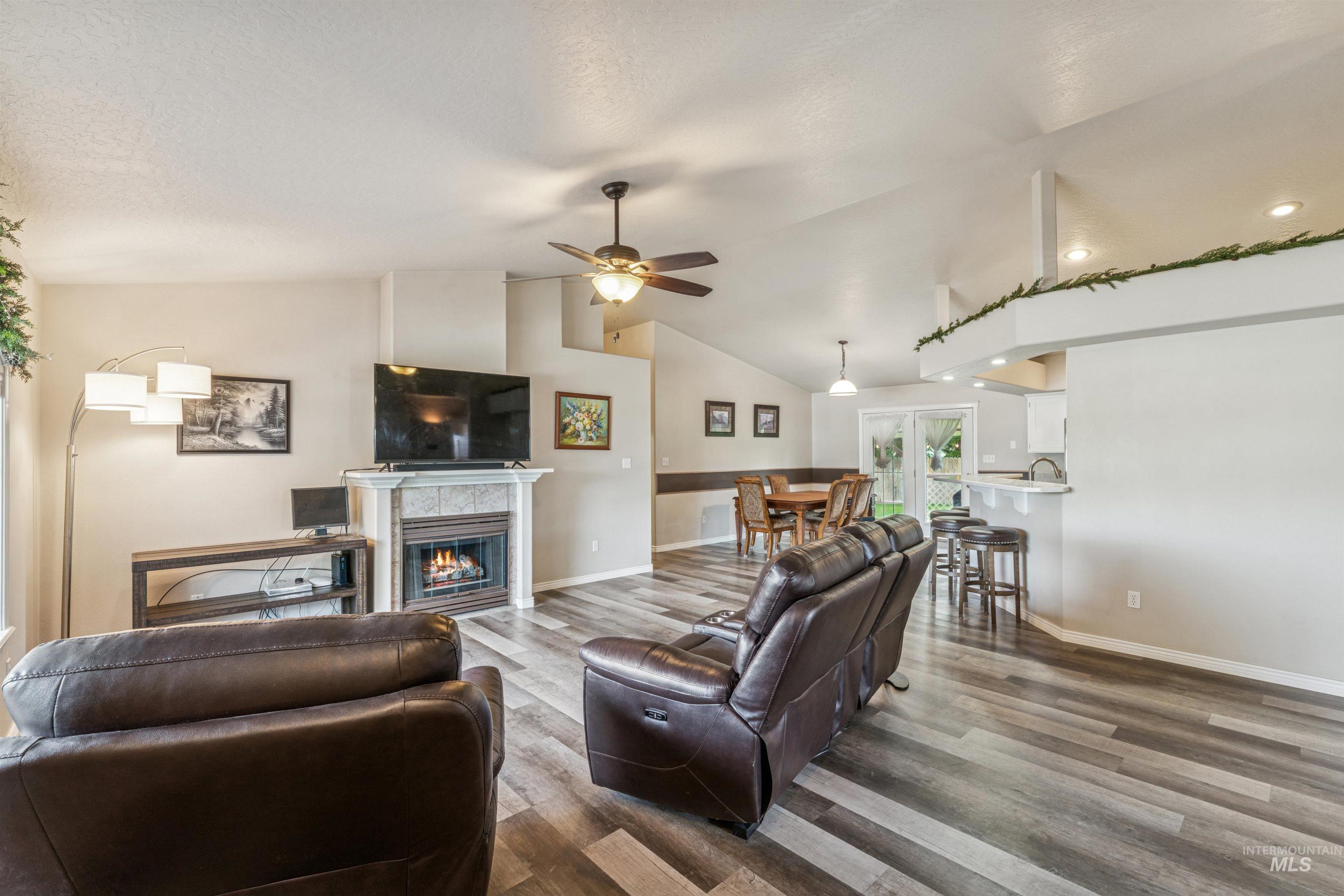 Living room with a tiled fireplace, wood finished floors, vaulted ceiling, and a ceiling fan