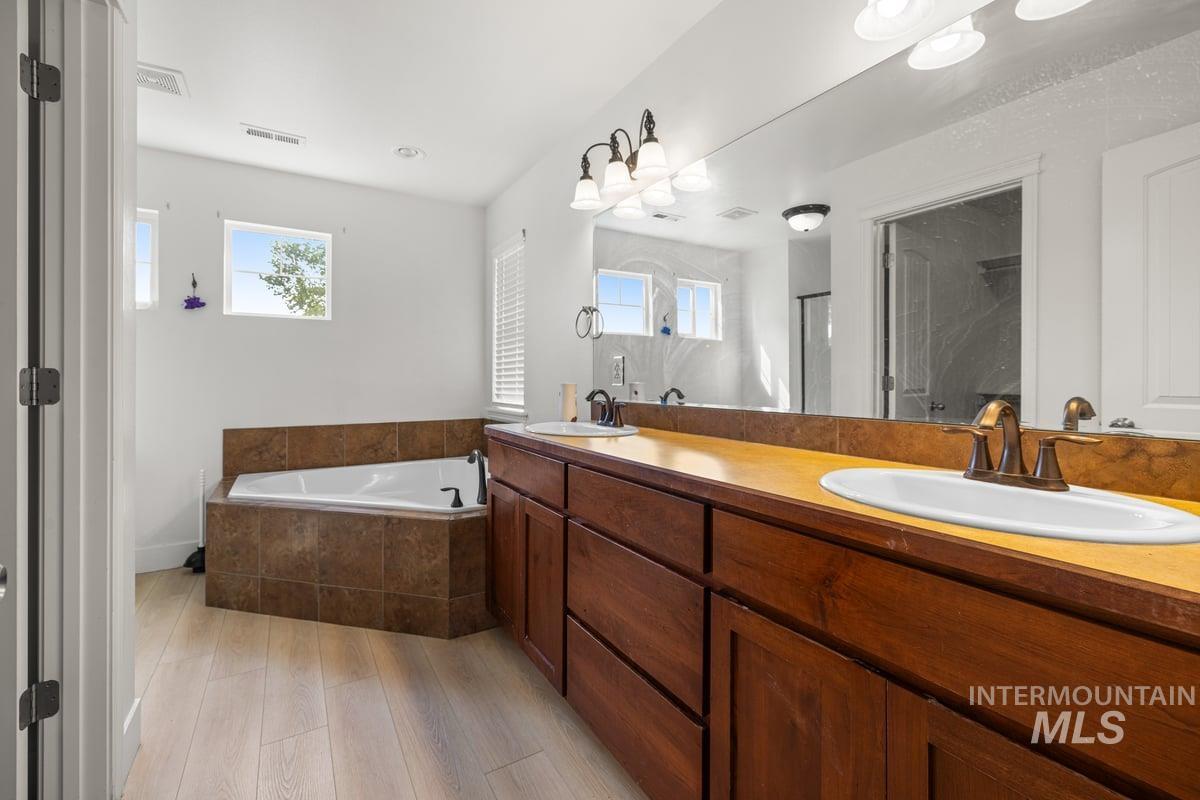 Full bathroom featuring a bath, double vanity, a stall shower, and light wood-type flooring