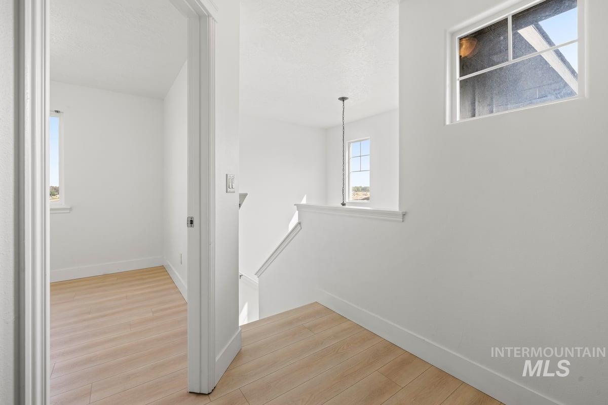 Corridor featuring an upstairs landing, light wood-style floors, and a textured ceiling