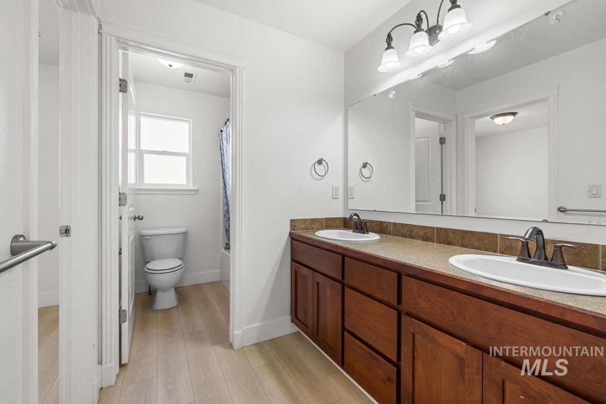 Full bath featuring shower / bathtub combination with curtain, double vanity, and light wood-type flooring