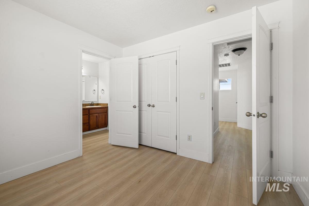 Unfurnished bedroom featuring light wood-type flooring, a closet, connected bathroom, and a textured ceiling