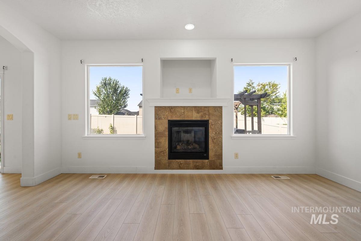 Unfurnished living room with a tiled fireplace, light wood-type flooring, recessed lighting, and a textured ceiling