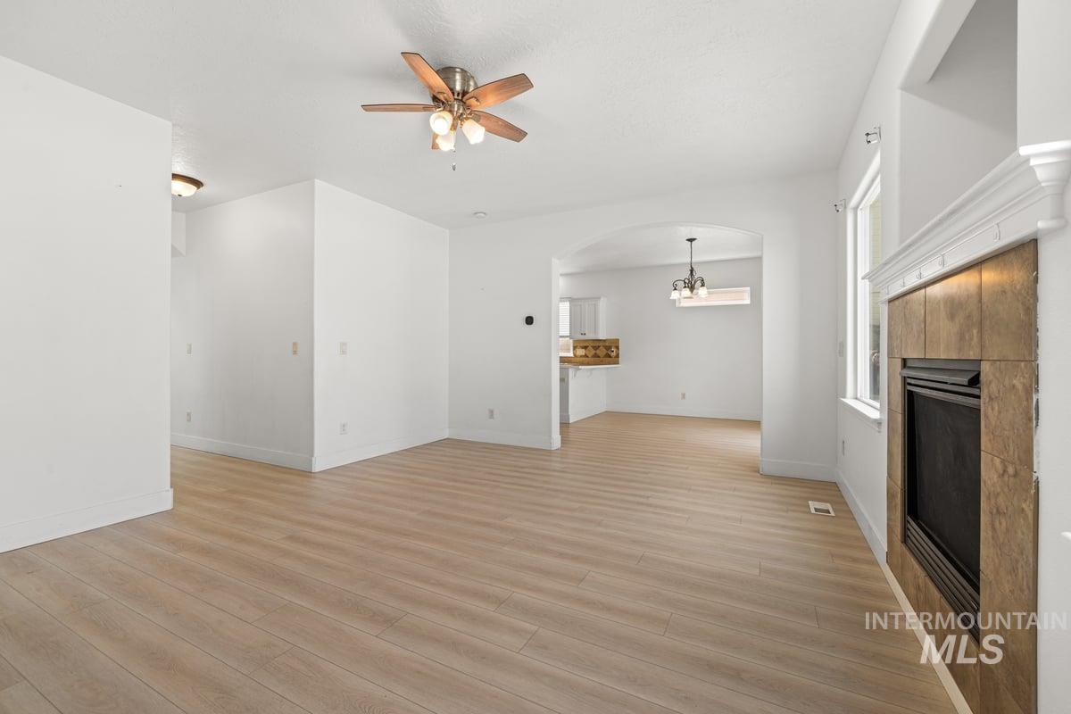 Unfurnished living room with light wood-style flooring, a tile fireplace, arched walkways, and a ceiling fan