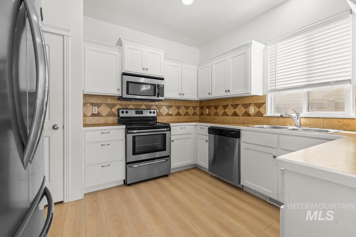 Kitchen featuring stainless steel appliances, white cabinets, and light countertops