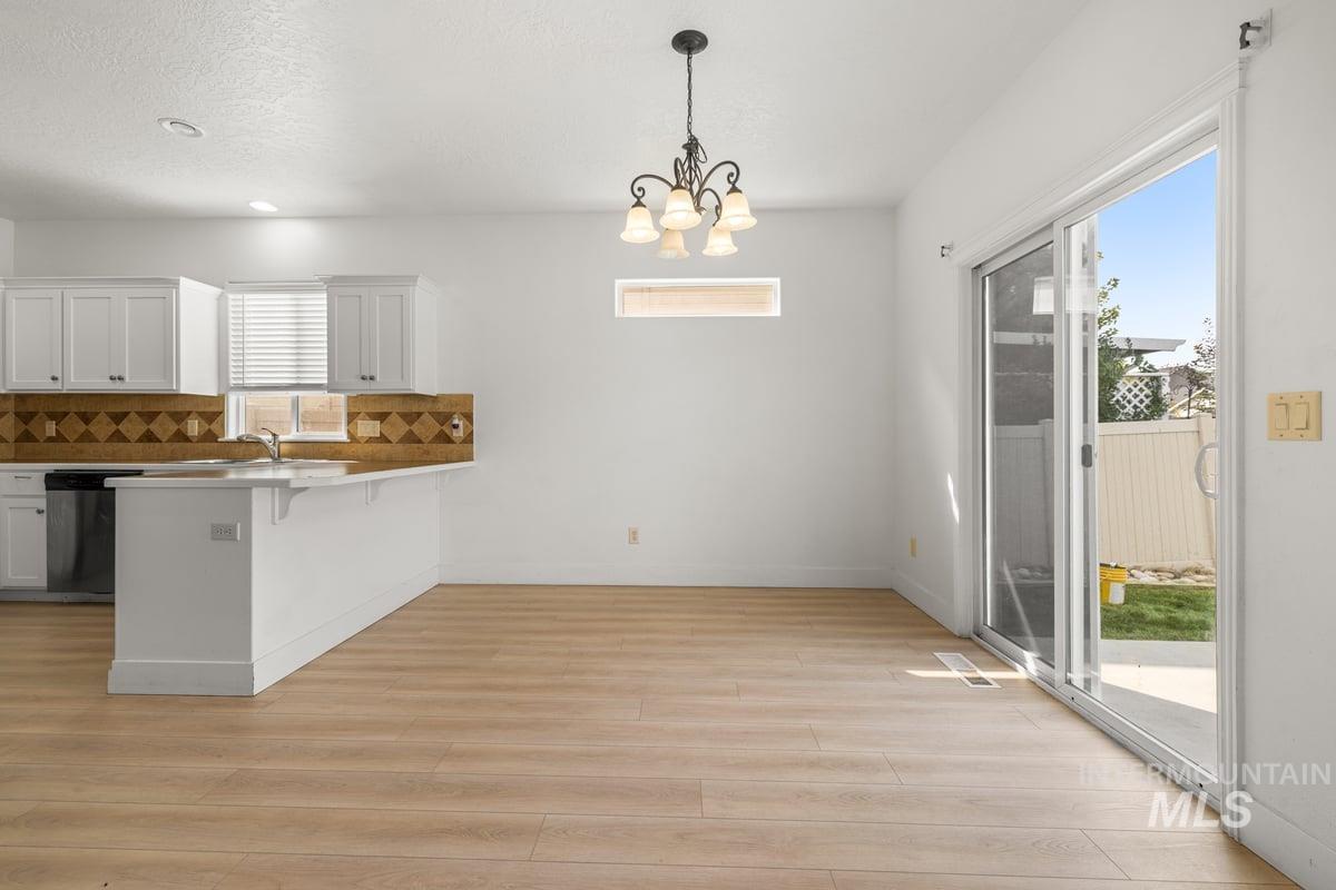 Kitchen with white cabinetry, tasteful backsplash, hanging light fixtures, a kitchen breakfast bar, and light wood-style flooring