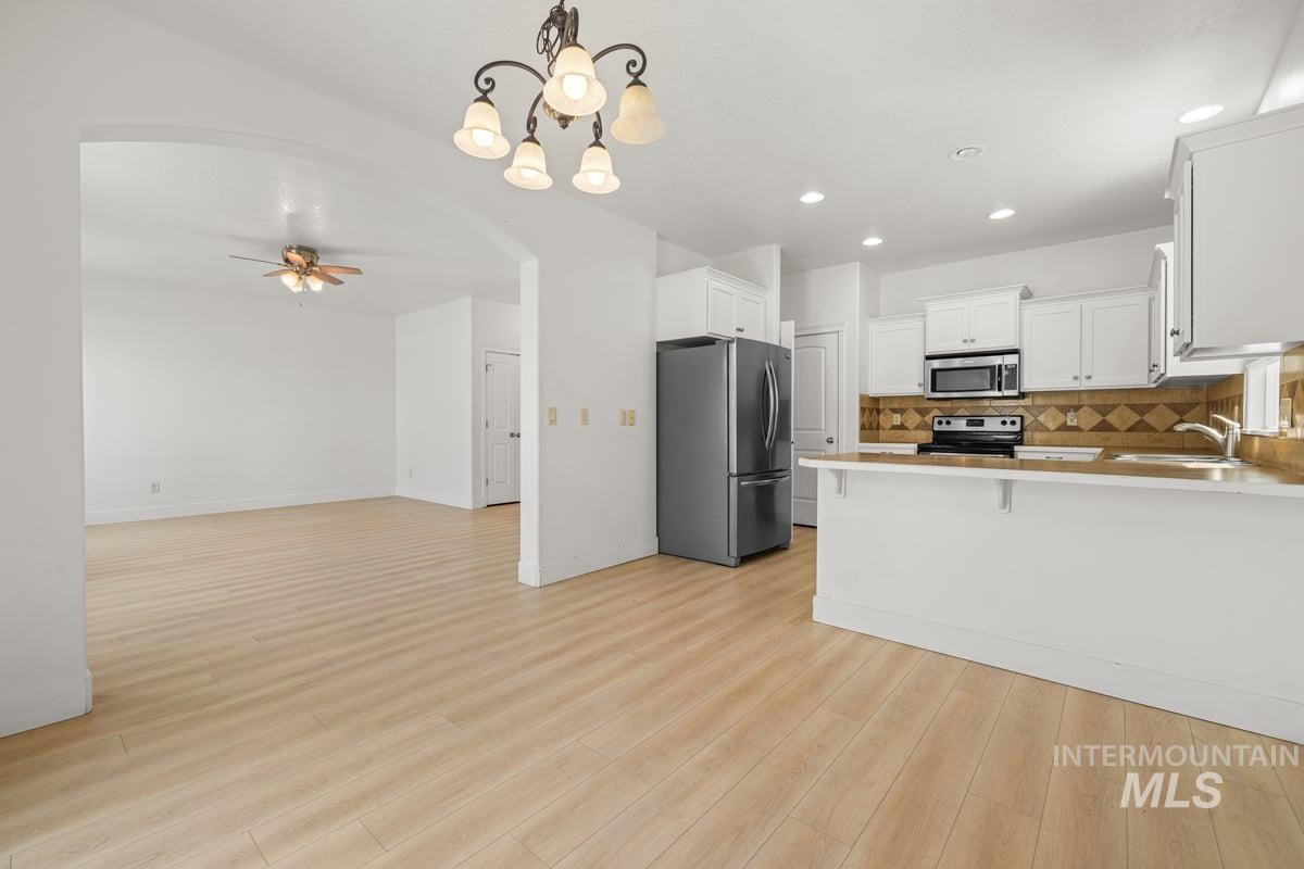 Kitchen with hanging light fixtures, arched walkways, stainless steel appliances, a chandelier, and decorative backsplash