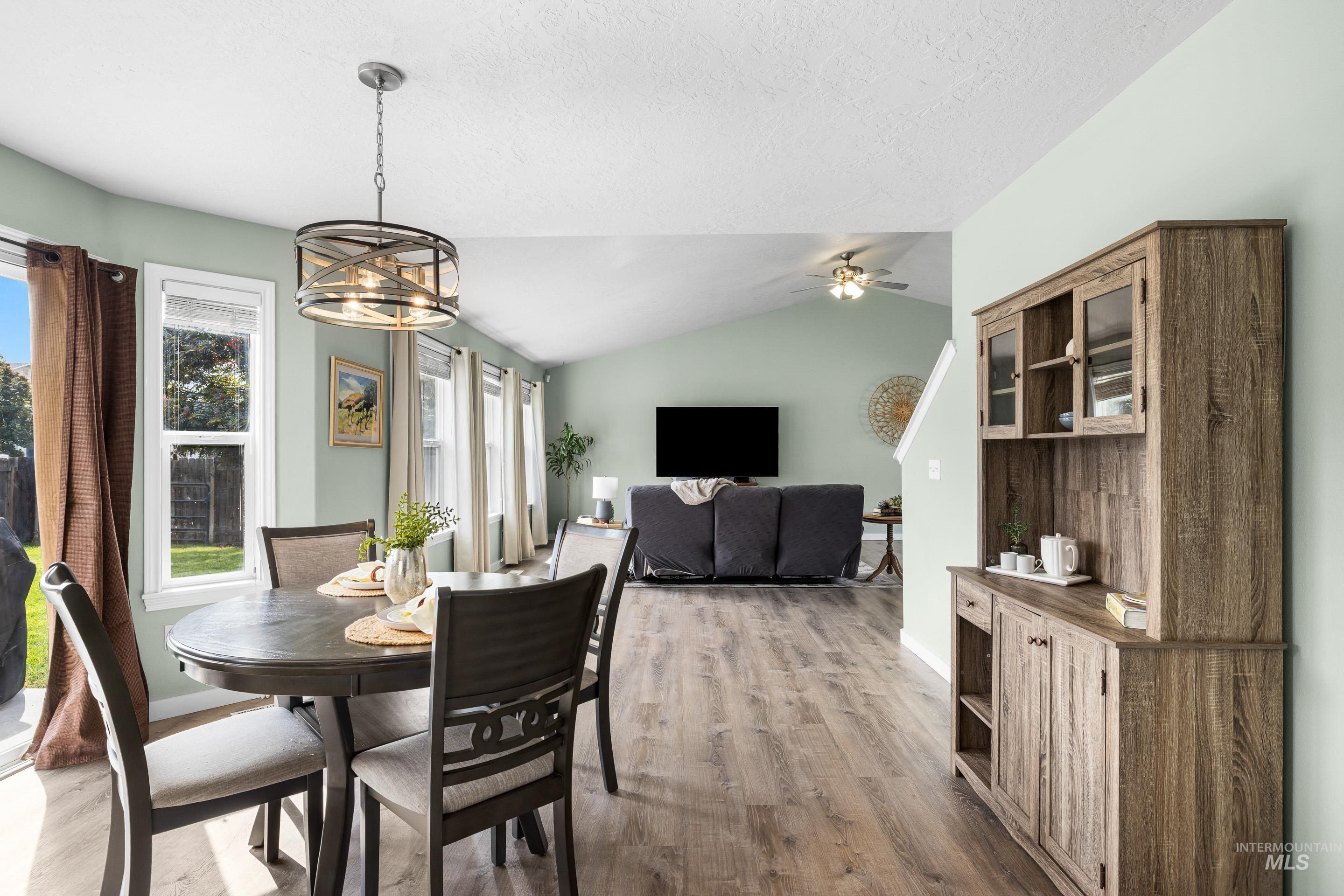 Dining area with lofted ceiling, light wood finished floors, a chandelier, and a textured ceiling