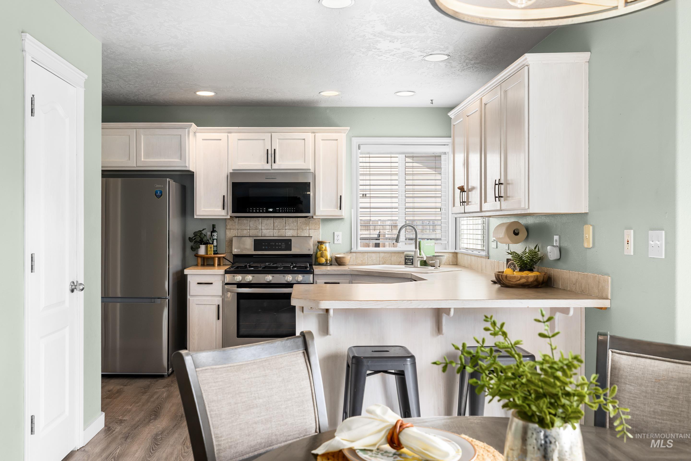 Kitchen with light countertops, white cabinetry, stainless steel appliances, a kitchen breakfast bar, and recessed lighting