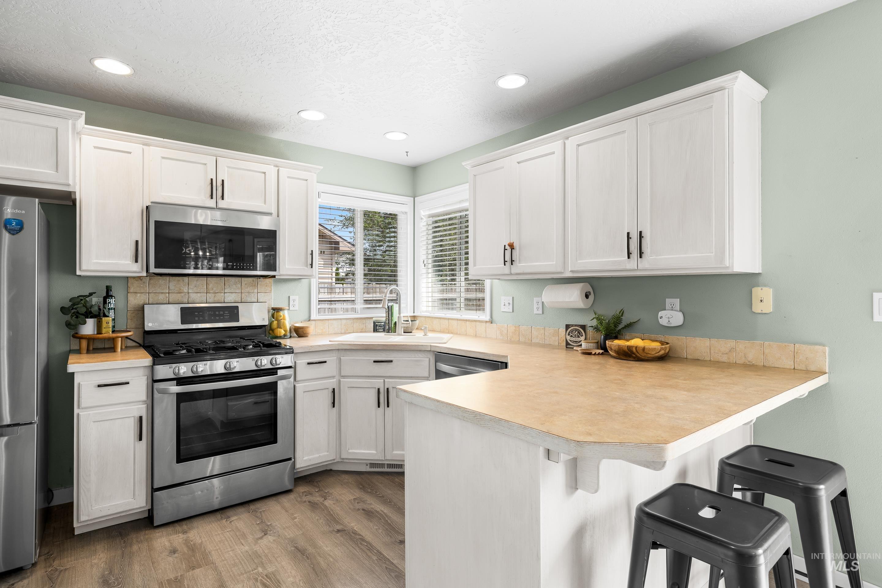 Kitchen with stainless steel appliances, white cabinets, light countertops, recessed lighting, and a textured ceiling