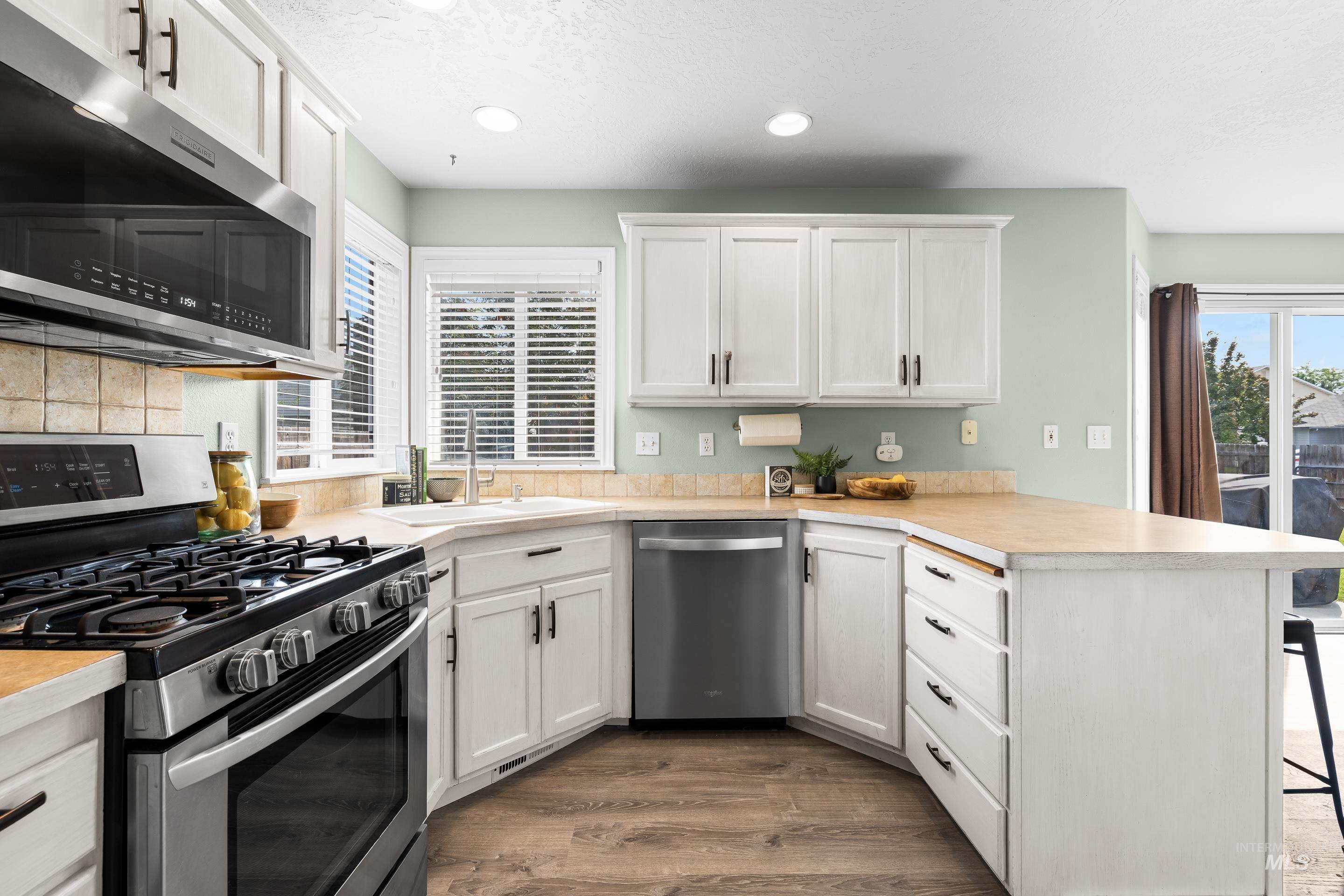 Kitchen with appliances with stainless steel finishes, white cabinetry, light countertops, a peninsula, and a textured ceiling