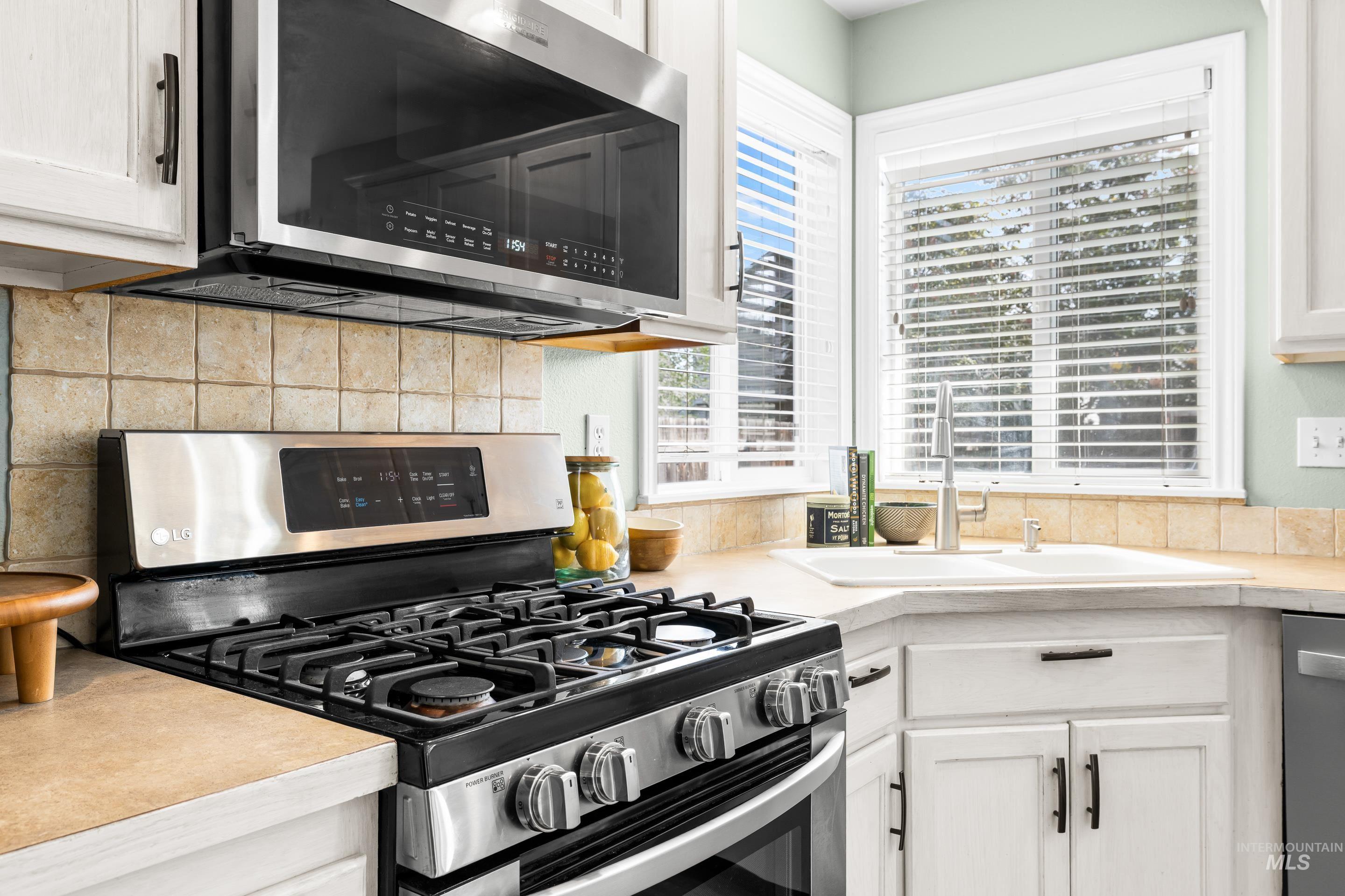 Kitchen featuring stainless steel appliances, white cabinetry, light countertops, and decorative backsplash