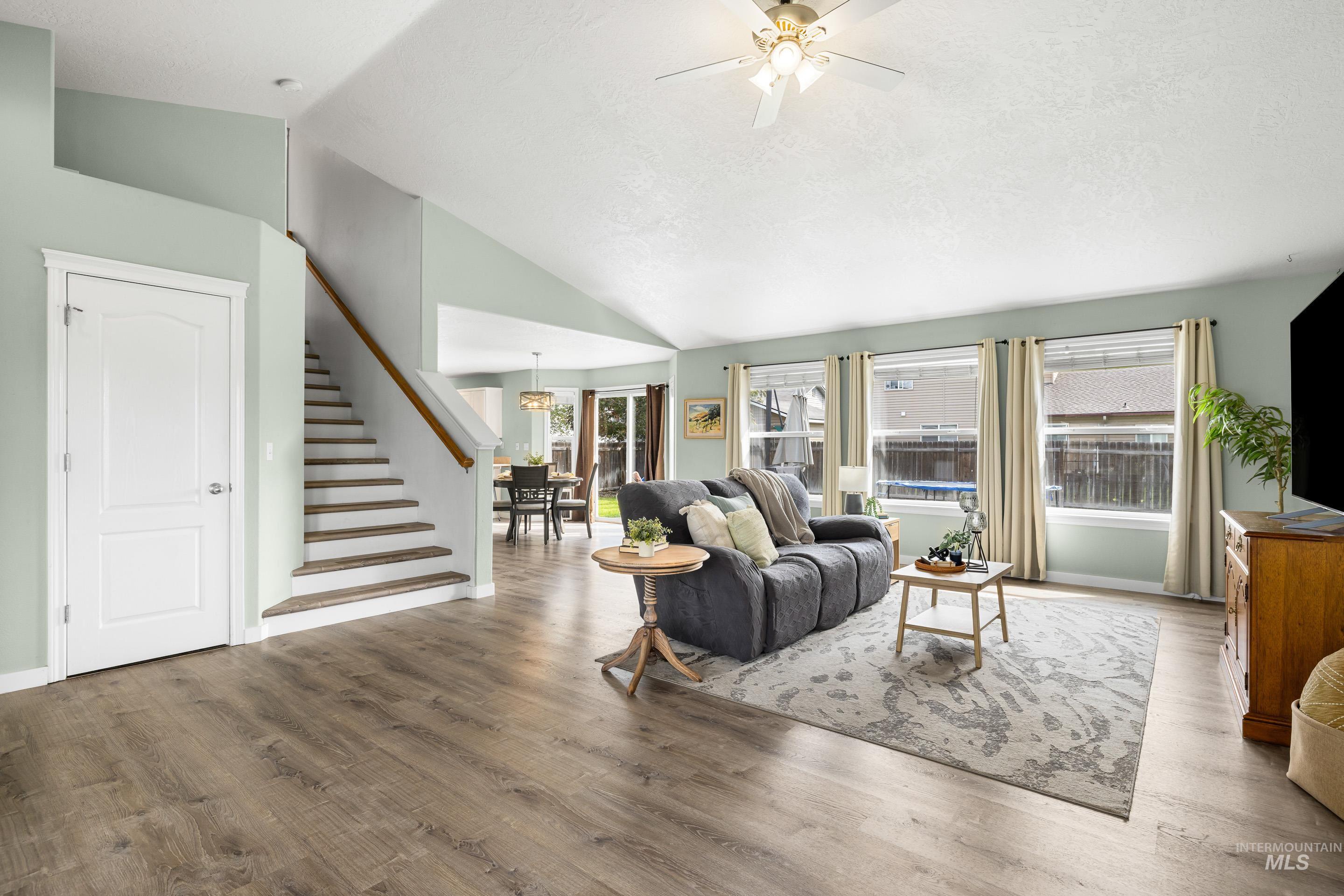Living room with wood finished floors, stairs, high vaulted ceiling, and a ceiling fan