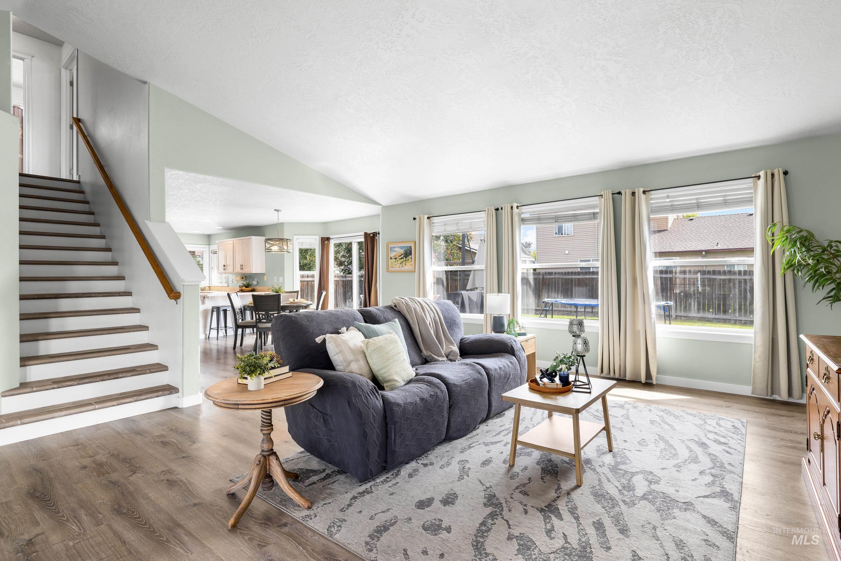 Living area with plenty of natural light, stairway, light wood-style flooring, lofted ceiling, and a textured ceiling