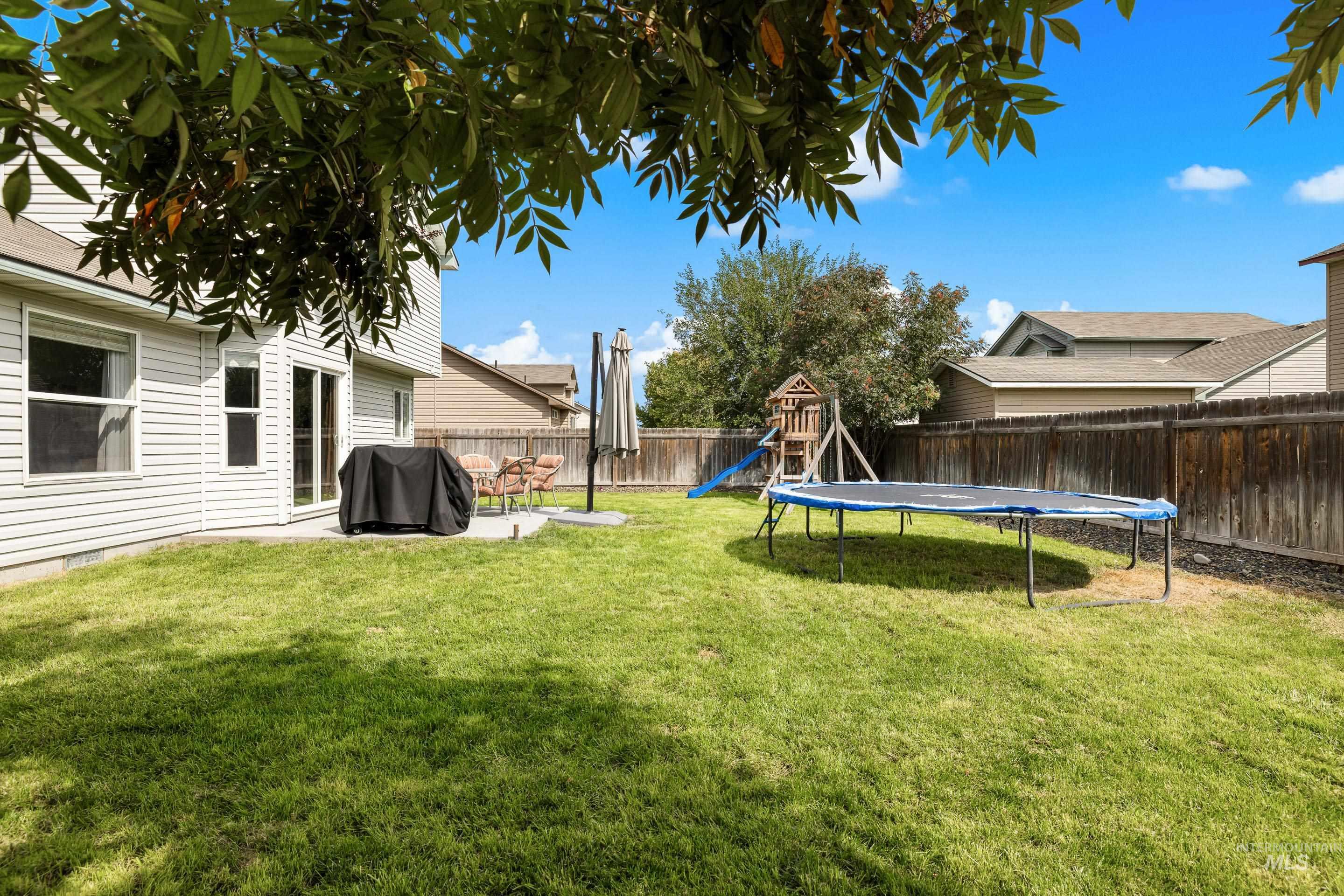 Fenced backyard with a playground, a patio, and a trampoline