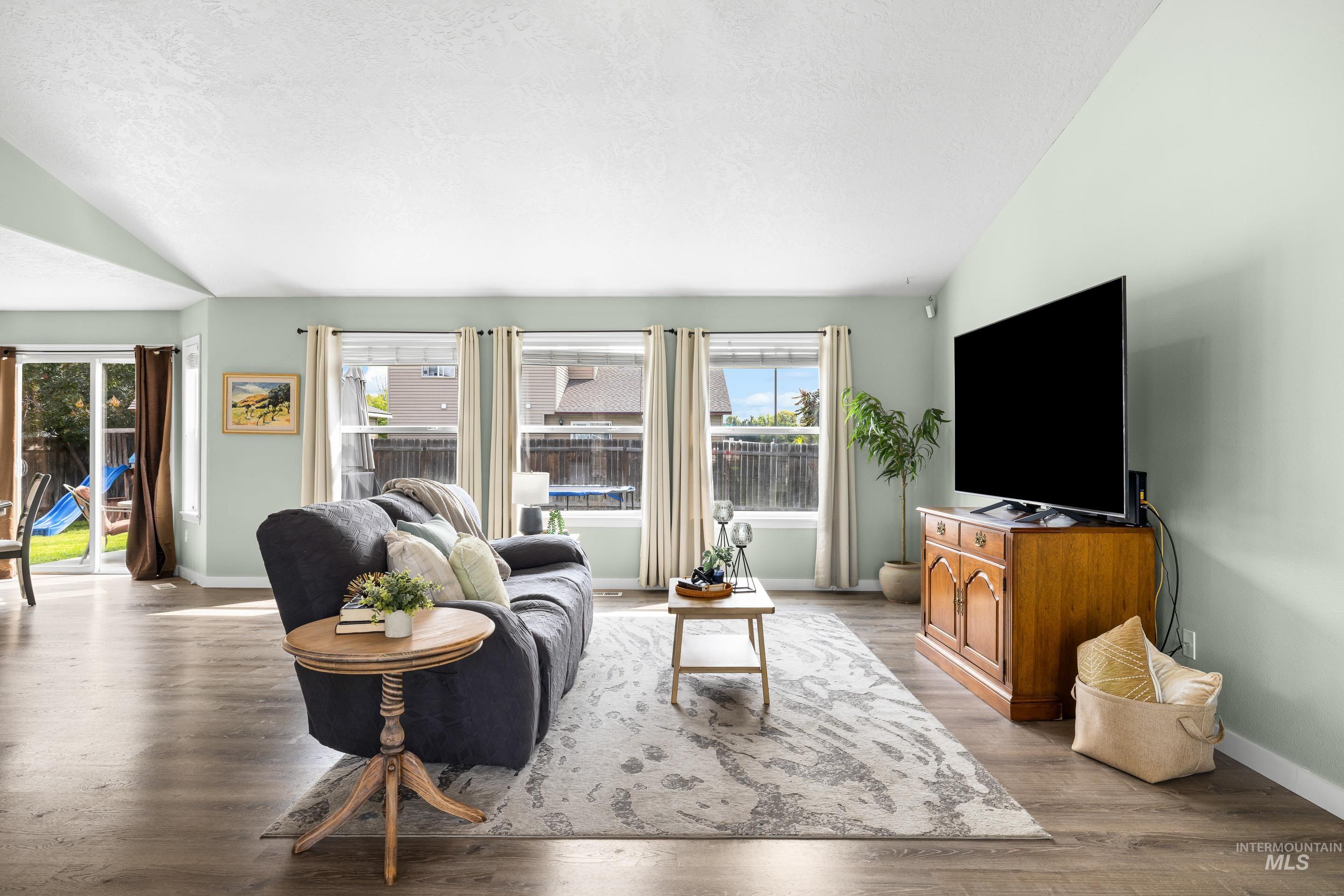 Living room with lofted ceiling, light wood finished floors, and a textured ceiling