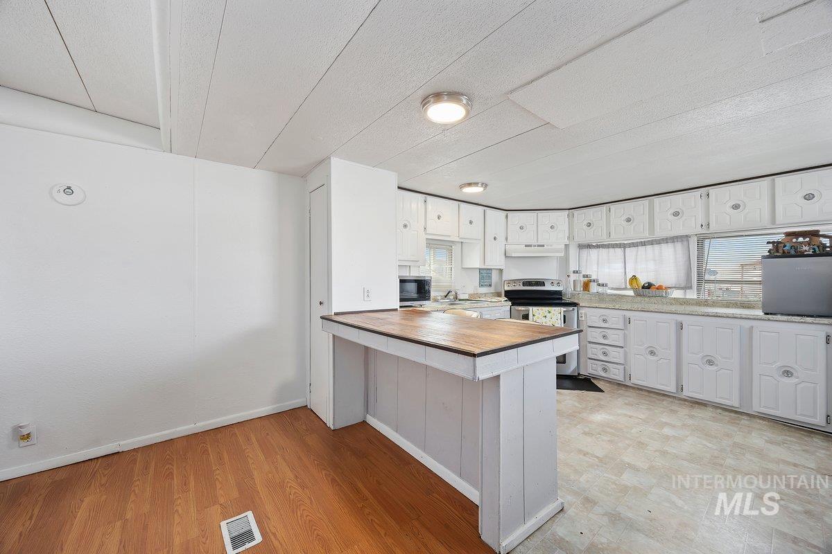 Kitchen with white cabinets, a peninsula, electric stove, butcher block countertops, and light wood-type flooring