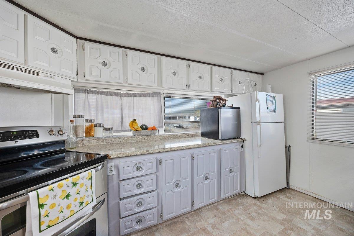 Kitchen with stainless steel appliances, healthy amount of natural light, a textured ceiling, under cabinet range hood, and white cabinets