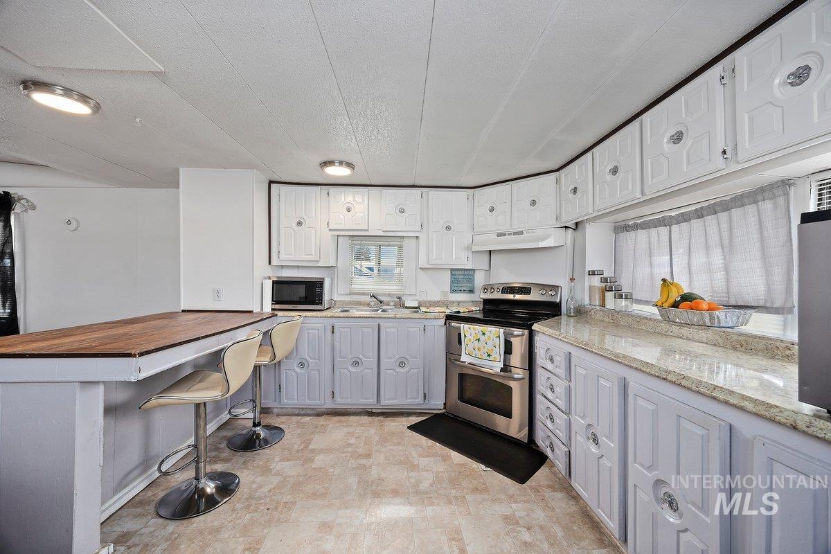 Kitchen featuring stainless steel appliances, butcher block counters, under cabinet range hood, a breakfast bar, and a textured ceiling