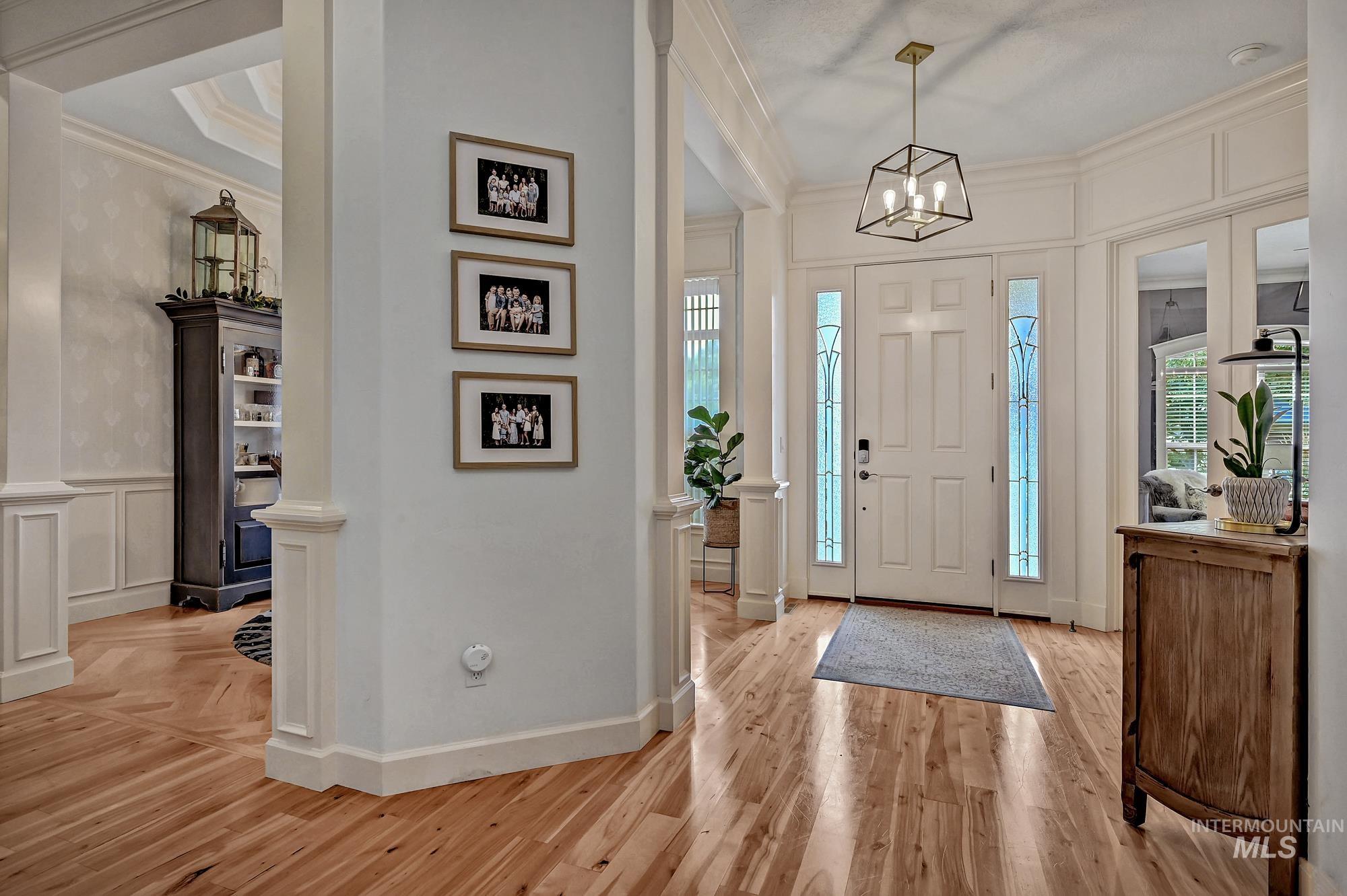 Foyer entrance featuring a decorative wall, plenty of natural light, ornamental molding, light wood-style floors, and a chandelier