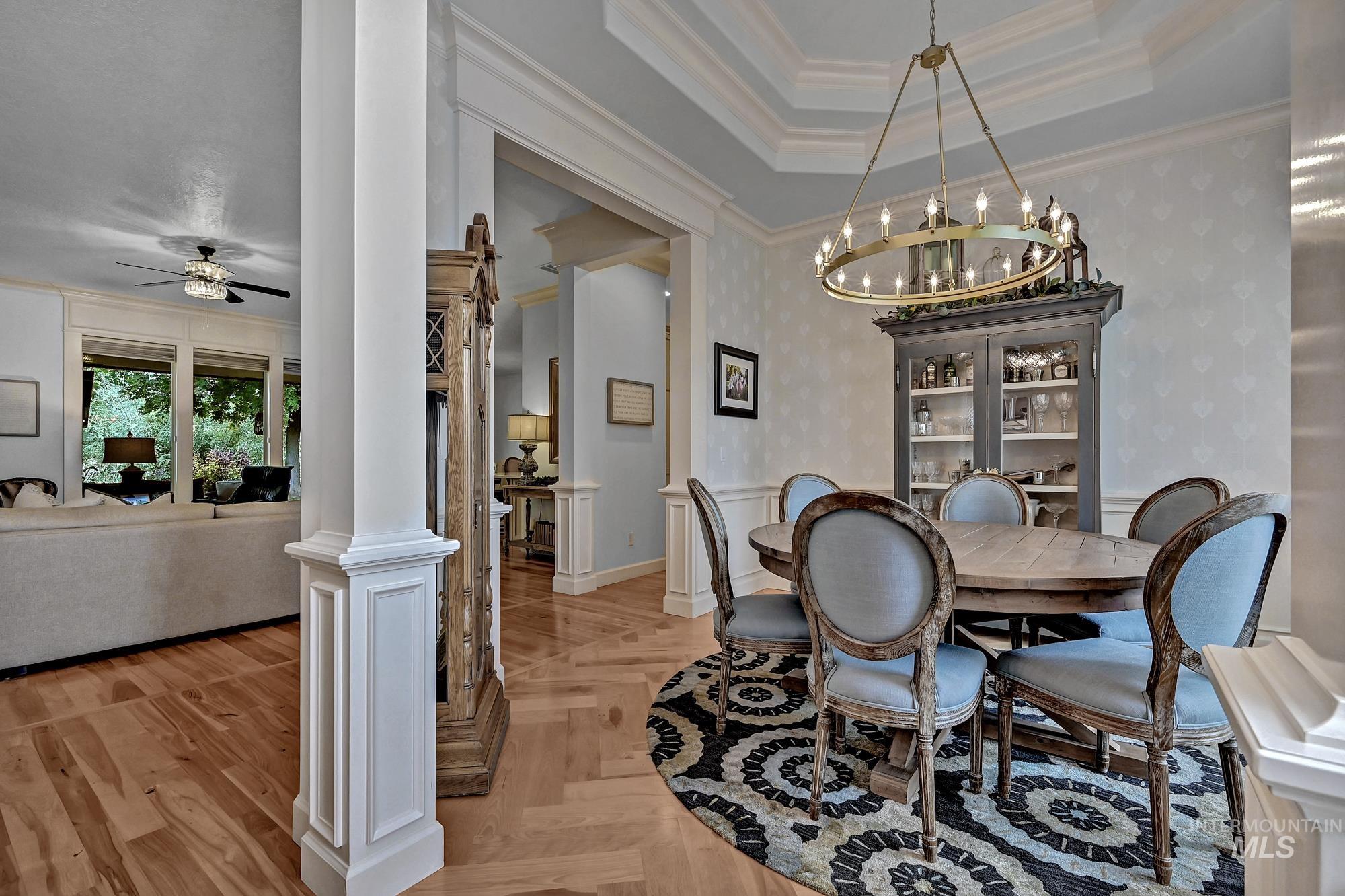 Dining area featuring ornamental molding, a raised ceiling, decorative columns, wallpapered walls, and a chandelier