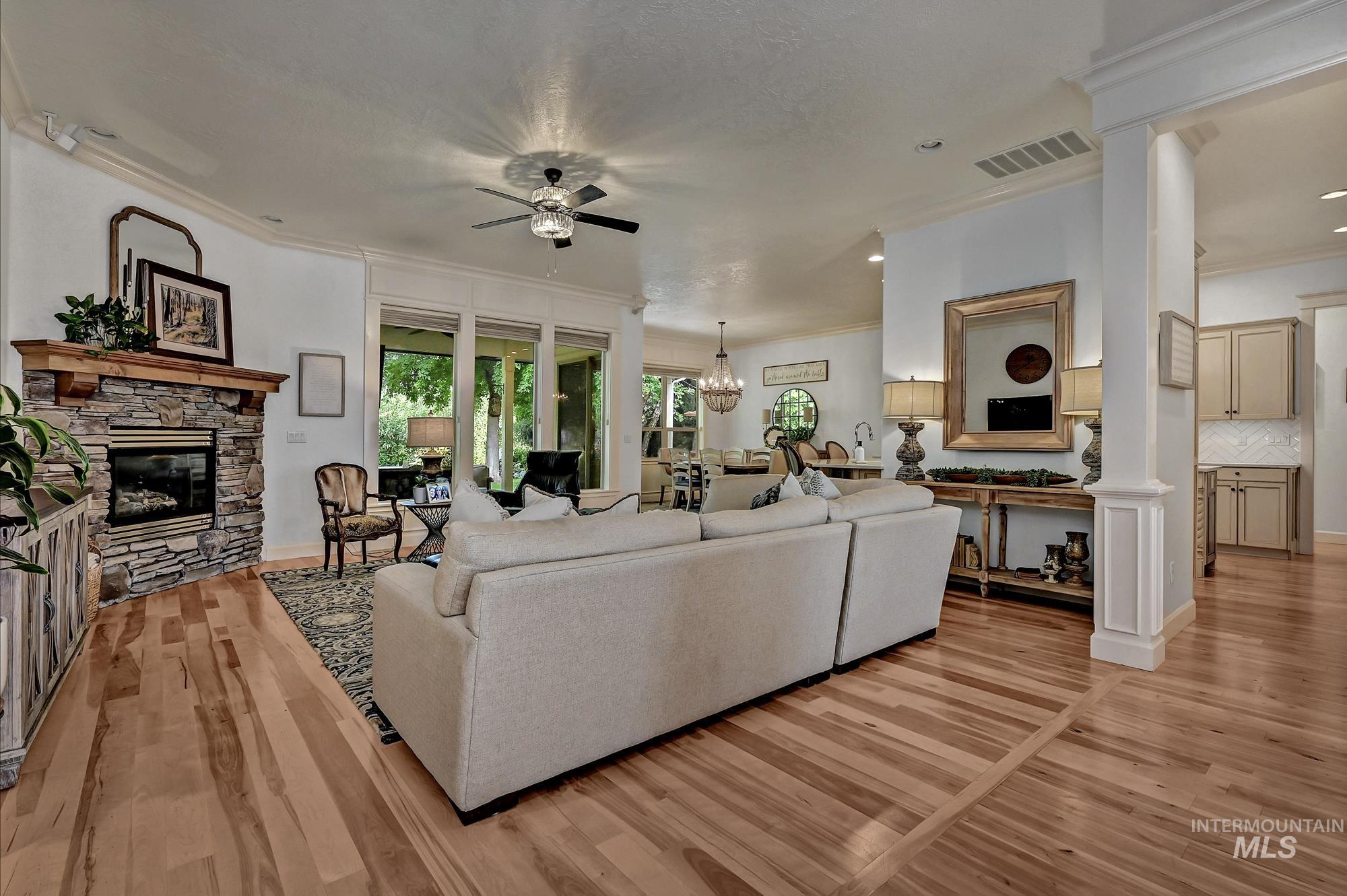 Living room featuring a fireplace, ceiling fan, ornamental molding, a chandelier, and light wood-type flooring