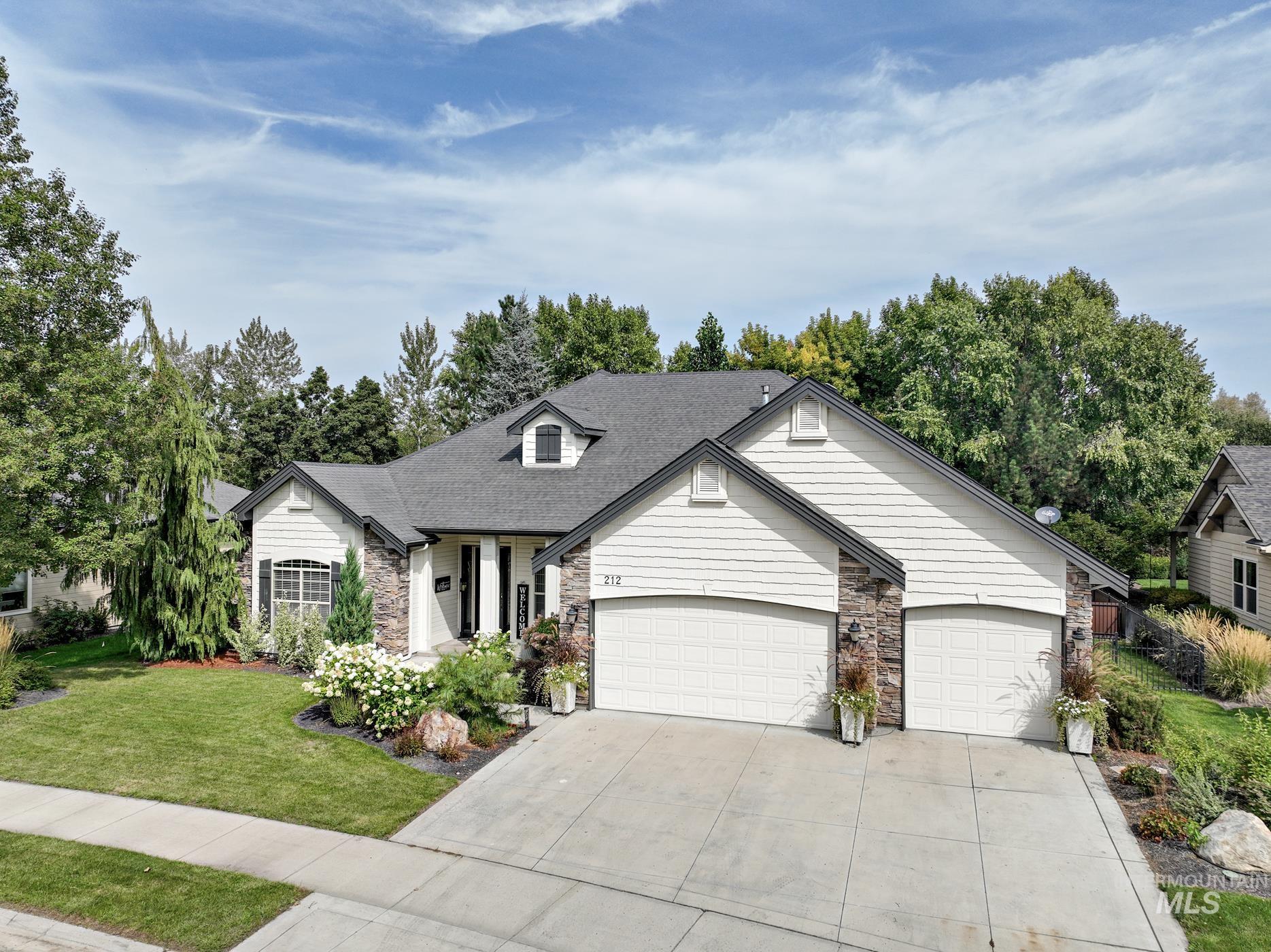 View of front facade with stone siding, driveway, a front yard, a garage, and a shingled roof