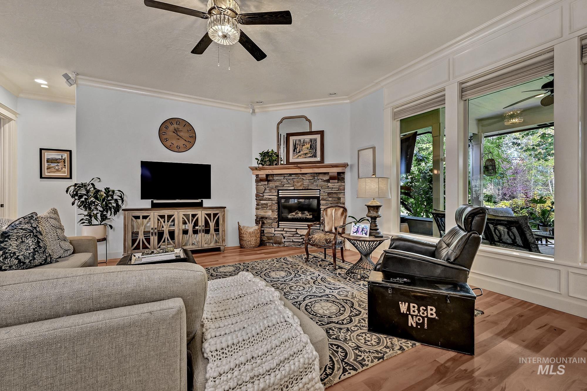 Living area with a ceiling fan, crown molding, wood finished floors, and a fireplace