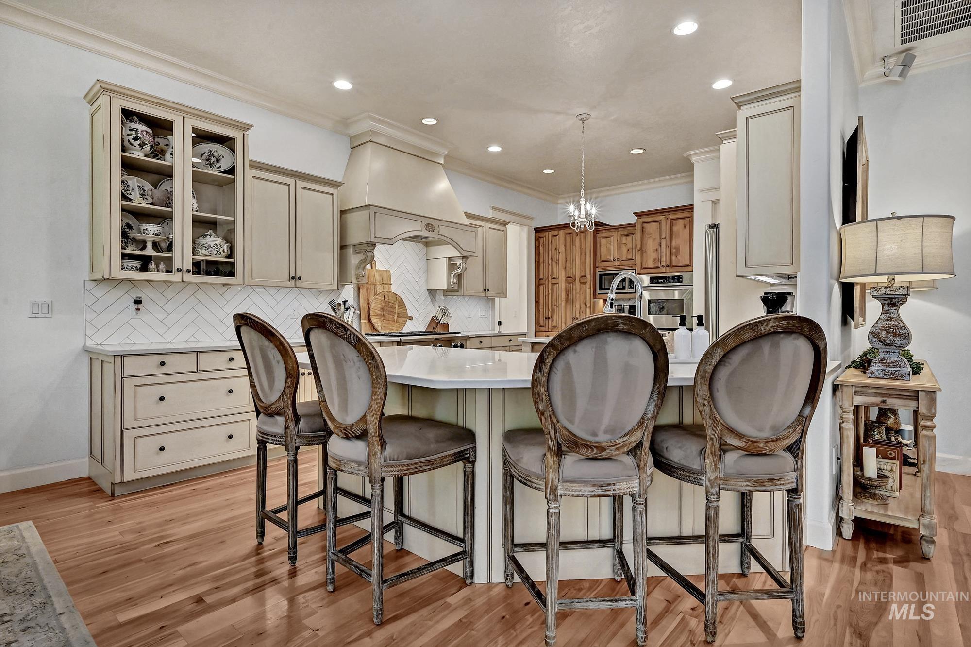 Kitchen with backsplash, cream cabinets, light wood-type flooring, pendant lighting, and glass insert cabinets