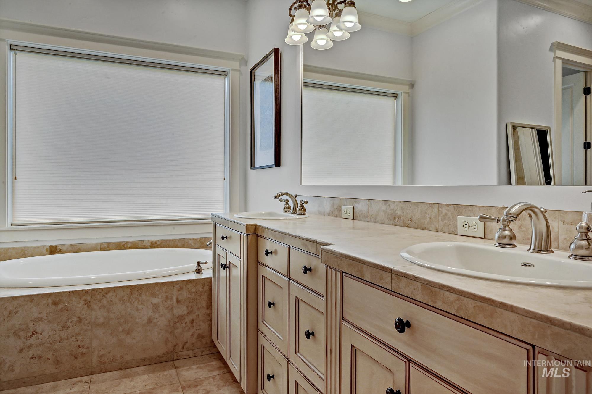 Full bath featuring double vanity, a bath, ornamental molding, travertine tile floors, and a chandelier