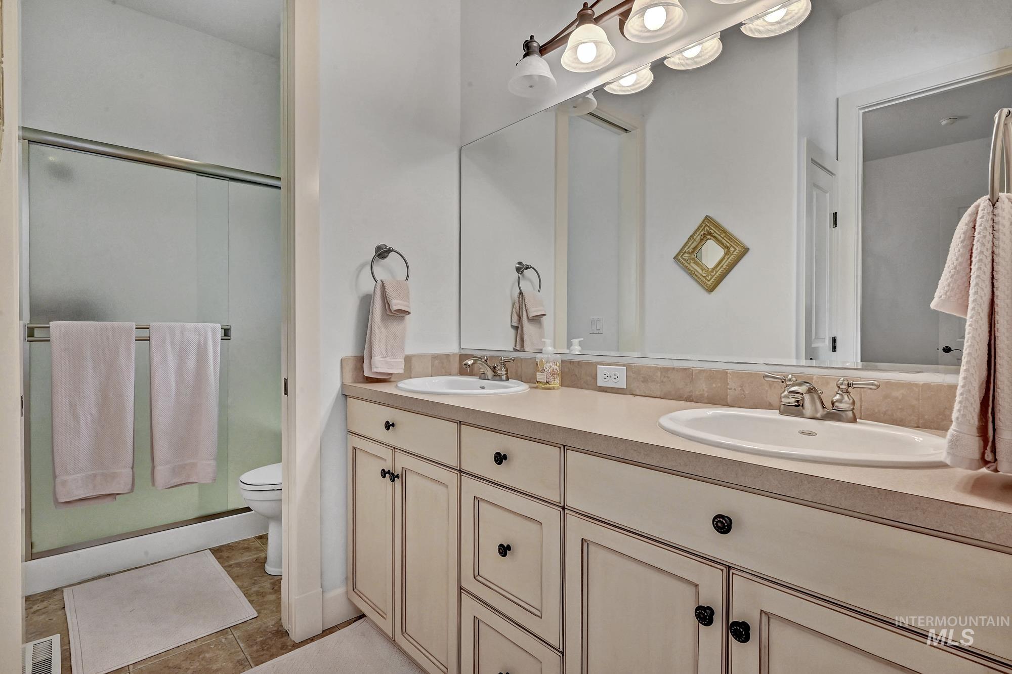 Bathroom featuring light tile patterned floors, double vanity, and a shower stall