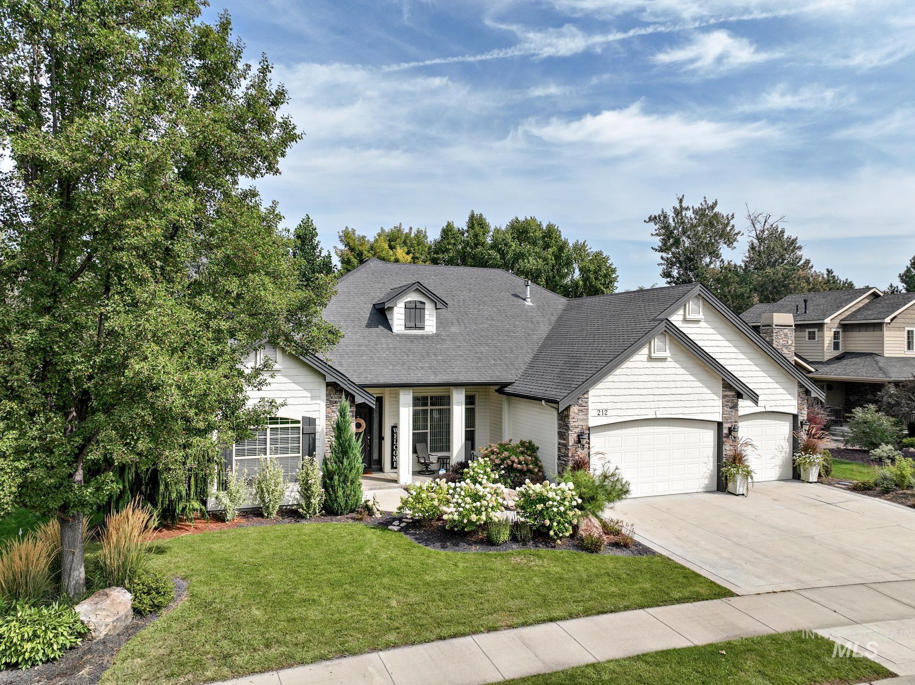 View of front of property featuring a front yard, concrete driveway, a garage, roof with shingles, and stone siding