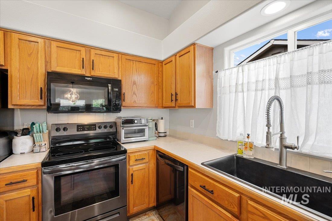 Kitchen featuring black appliances, light countertops, tasteful backsplash, and brown cabinetry