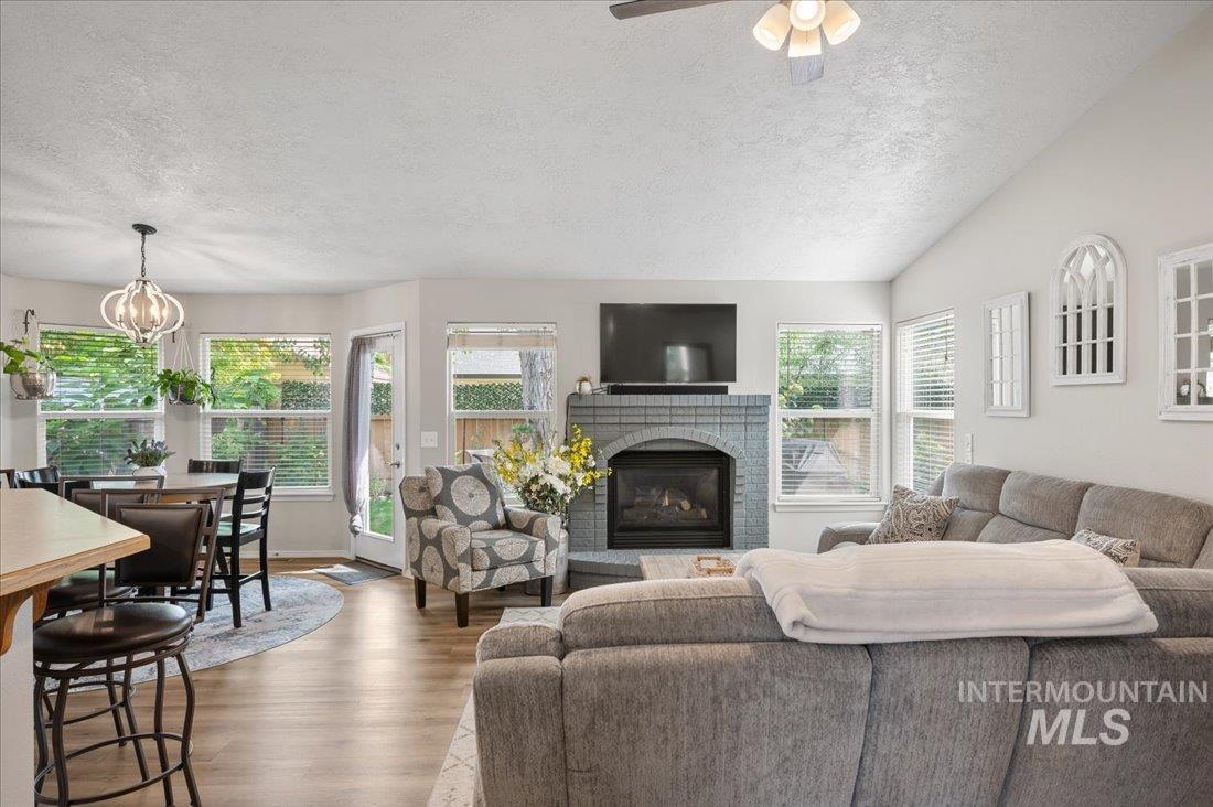 Living area with a textured ceiling, wood finished floors, a brick fireplace, lofted ceiling, and a chandelier