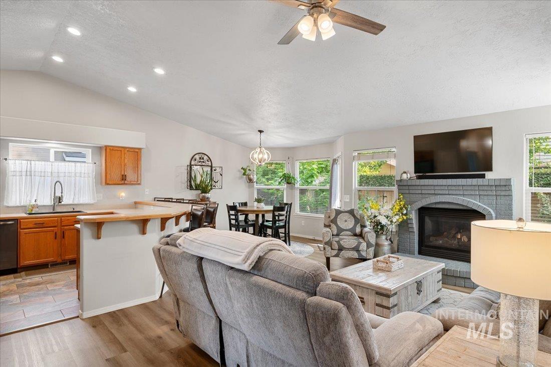 Living room with a brick fireplace, vaulted ceiling, light wood-style flooring, recessed lighting, and a textured ceiling