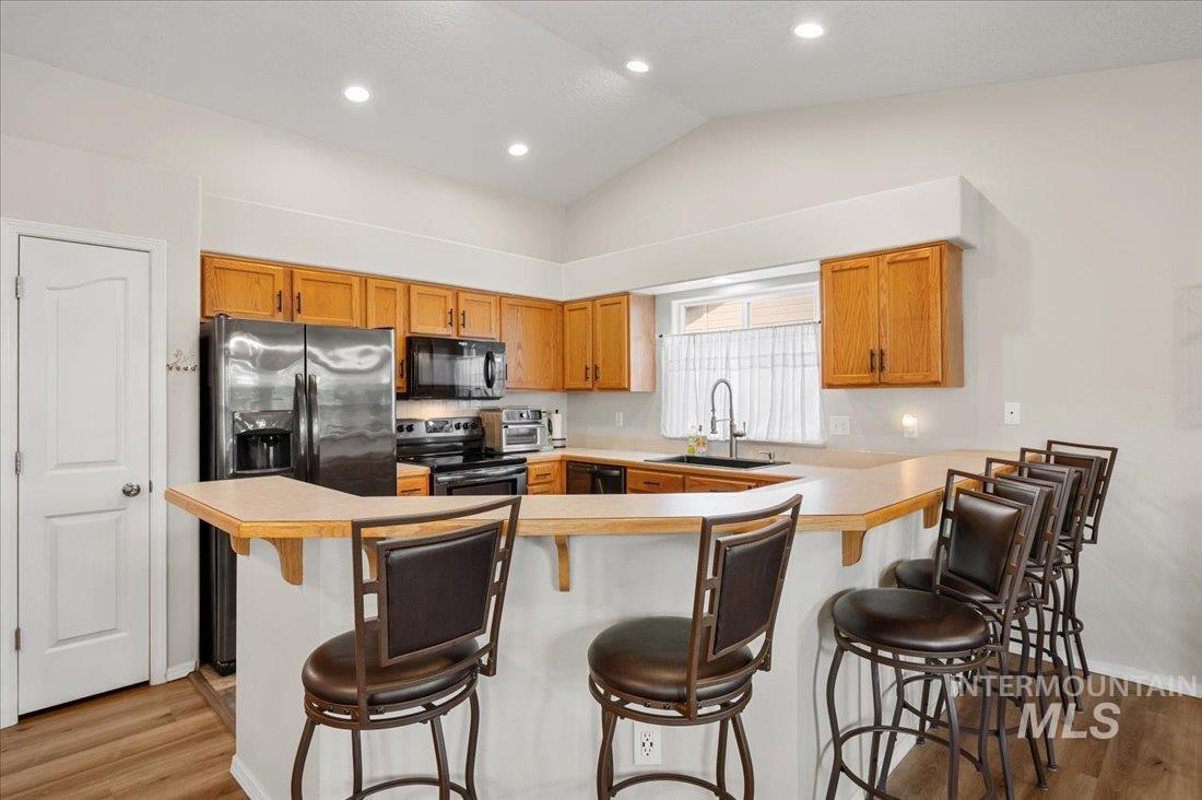Kitchen with light countertops, light wood-type flooring, brown cabinetry, black appliances, and lofted ceiling