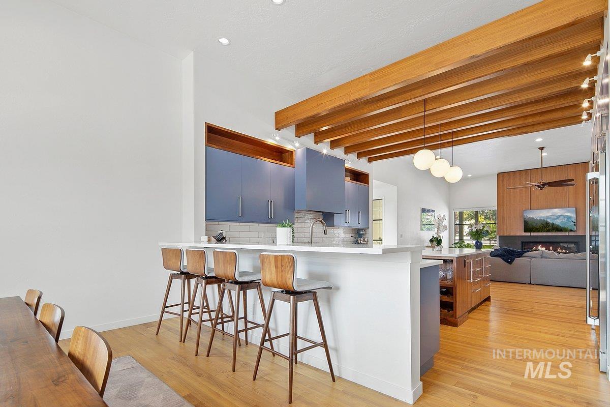Kitchen with a breakfast bar, beamed ceiling, pendant lighting, decorative backsplash, and open floor plan
