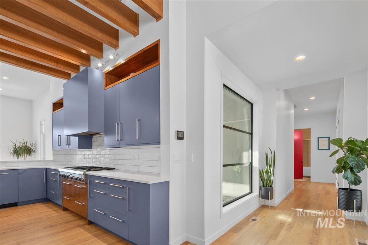 Kitchen with wall chimney range hood, stainless steel gas cooktop, light wood-type flooring, tasteful backsplash, and light countertops