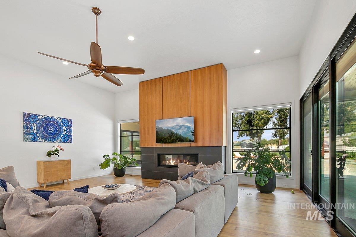 Living room featuring a tiled fireplace, light wood-type flooring, ceiling fan, and recessed lighting