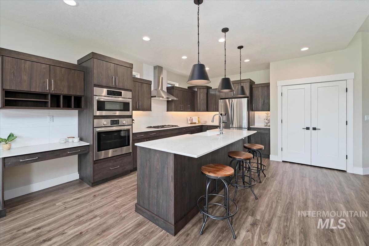 Kitchen featuring dark brown cabinets, a kitchen breakfast bar, stainless steel appliances, a center island with sink, and recessed lighting